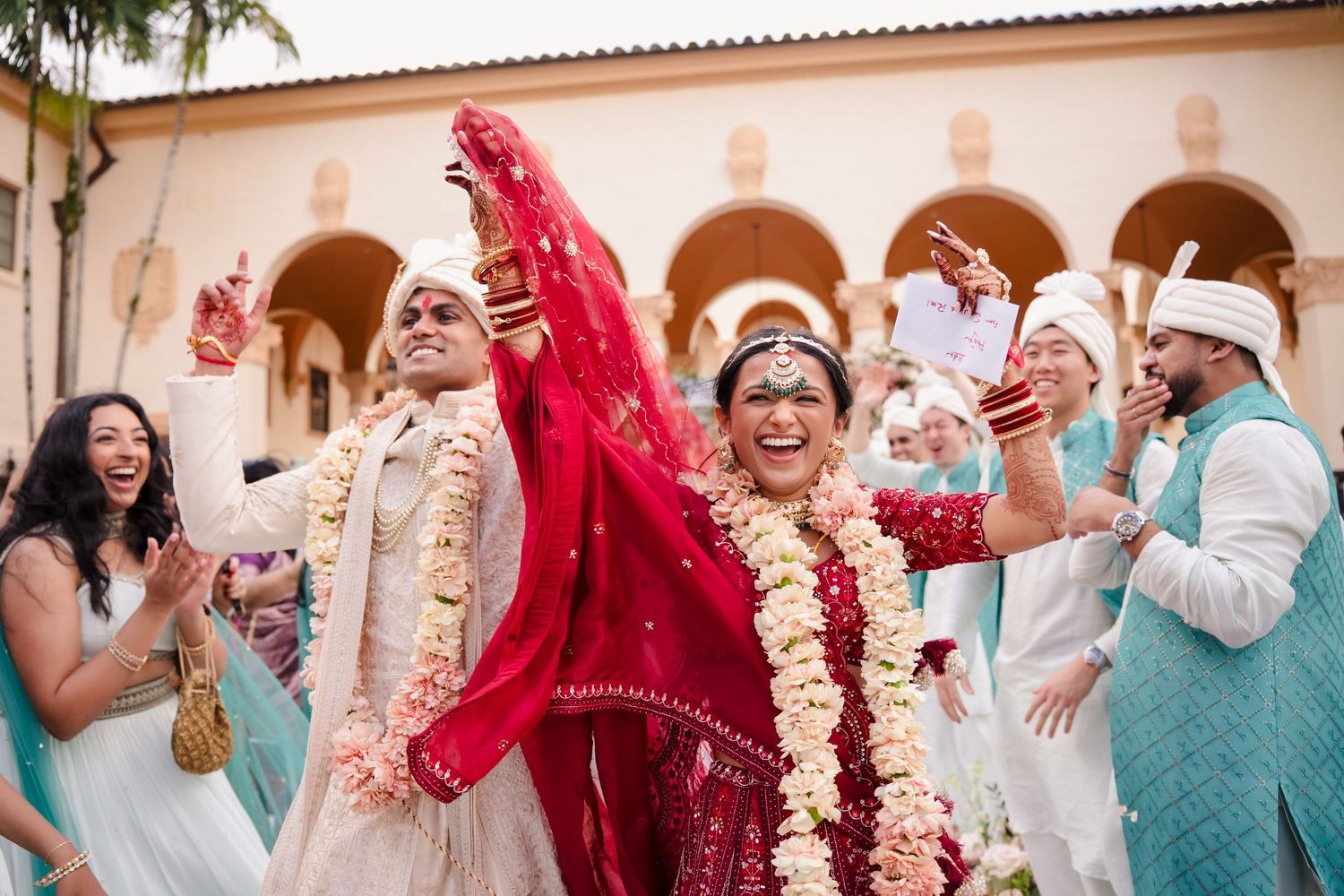 Vibrant South Asian wedding celebration with joyous guests in traditional attire at an elegant arched venue.