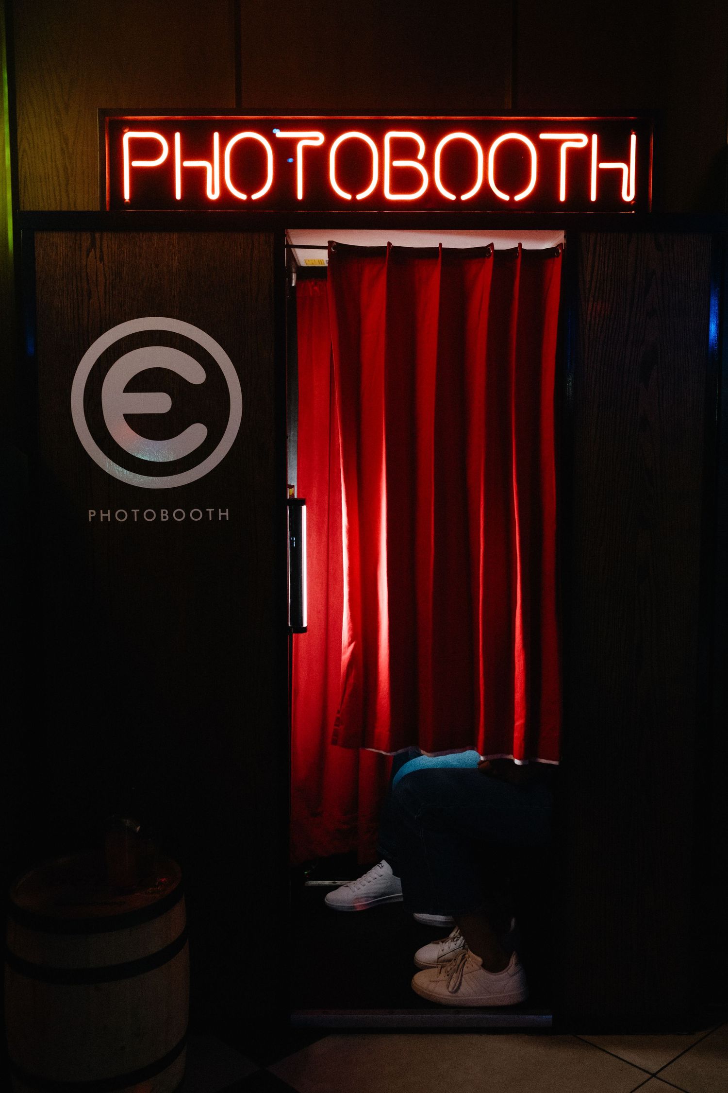 Red neon photobooth sign illuminating dark space with red curtain and circular logo.
