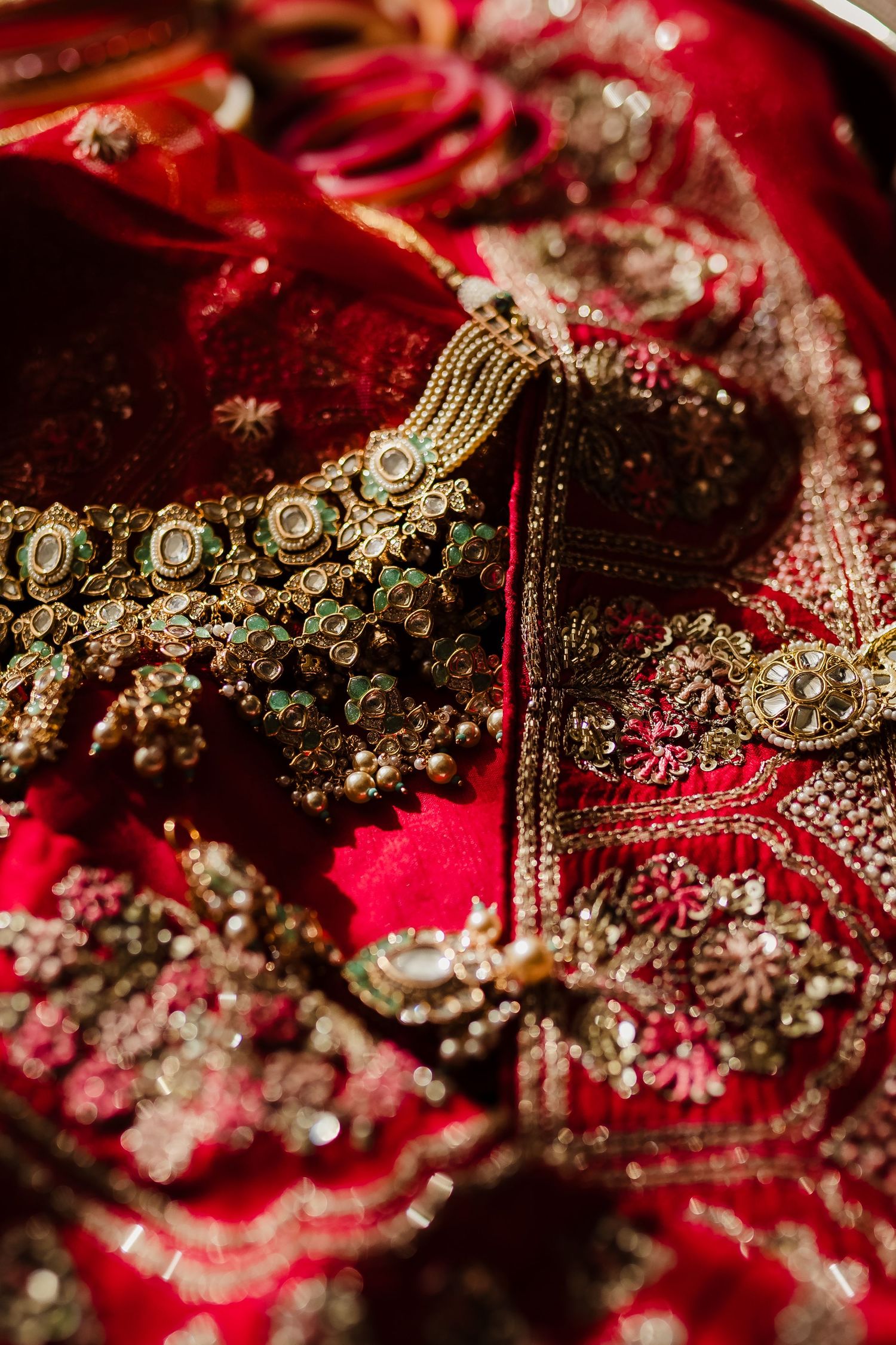 Ornate gold and pearl Indian bridal jewelry displayed on richly embroidered red fabric with traditional designs.