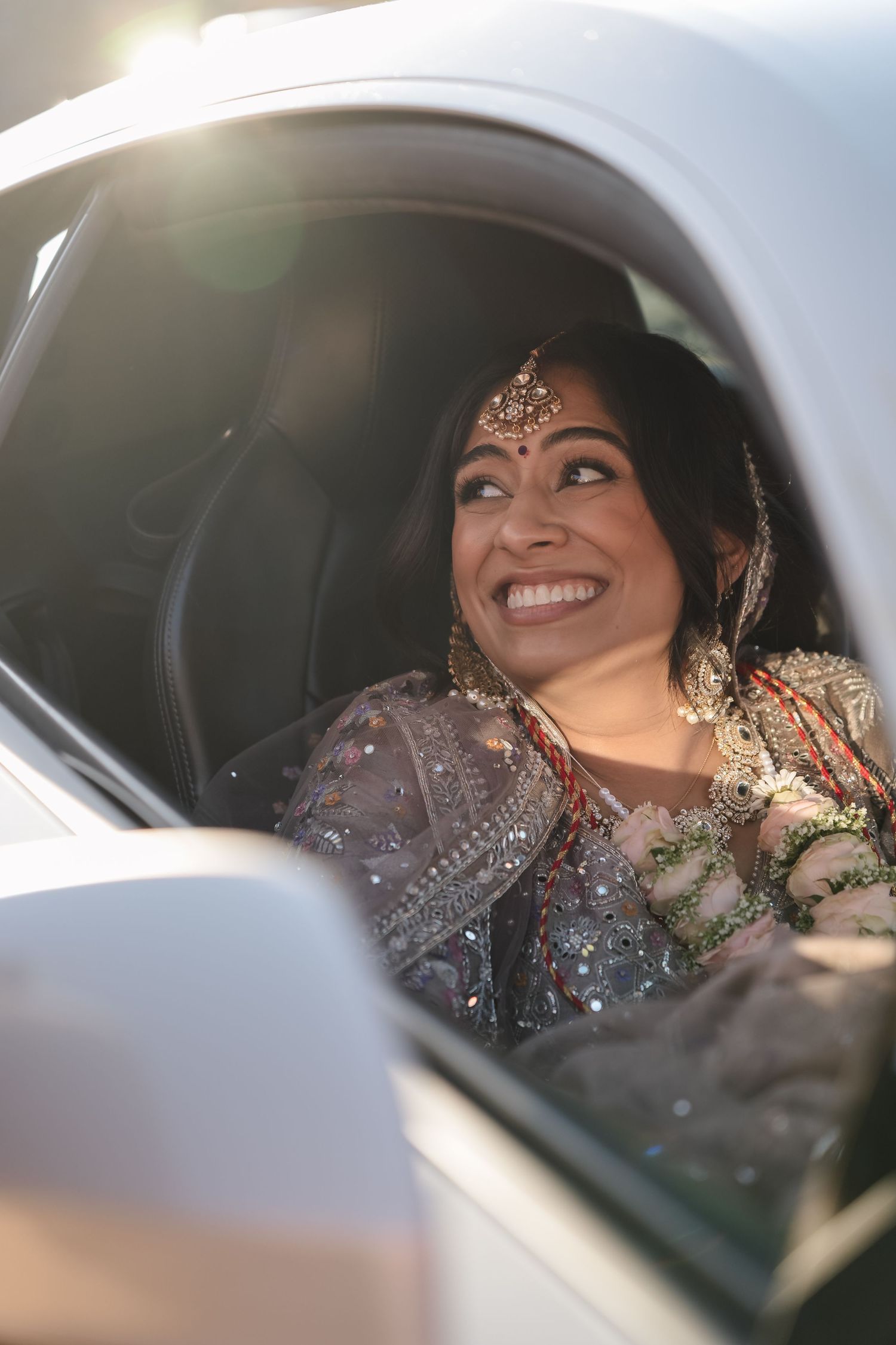 A joyful moment captured through a car window showing sparkly South Asian wedding attire.