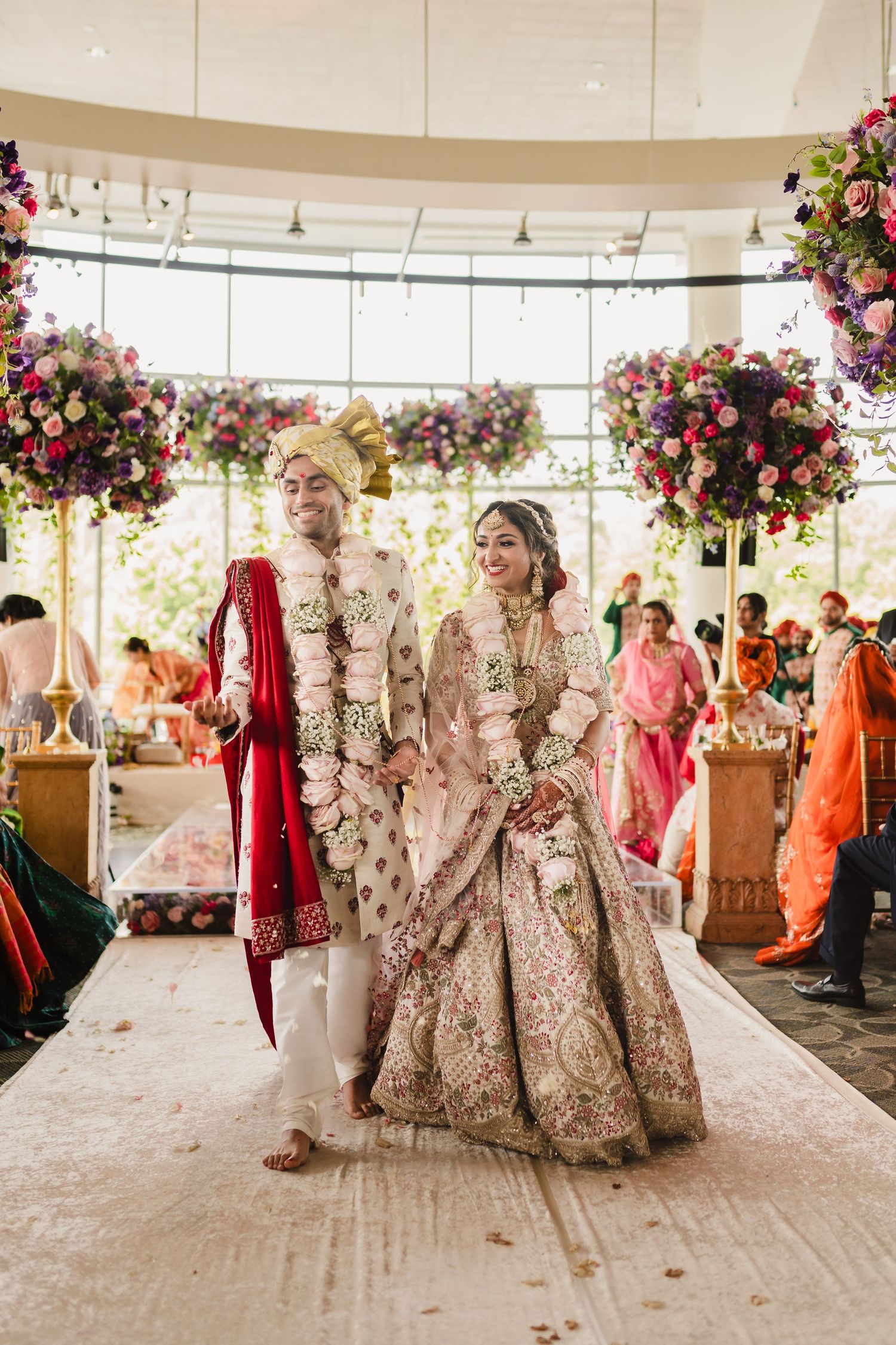 Luxurious Indian wedding ceremony with elegant floral decor featuring pink and red blooms under a bright modern venue.
