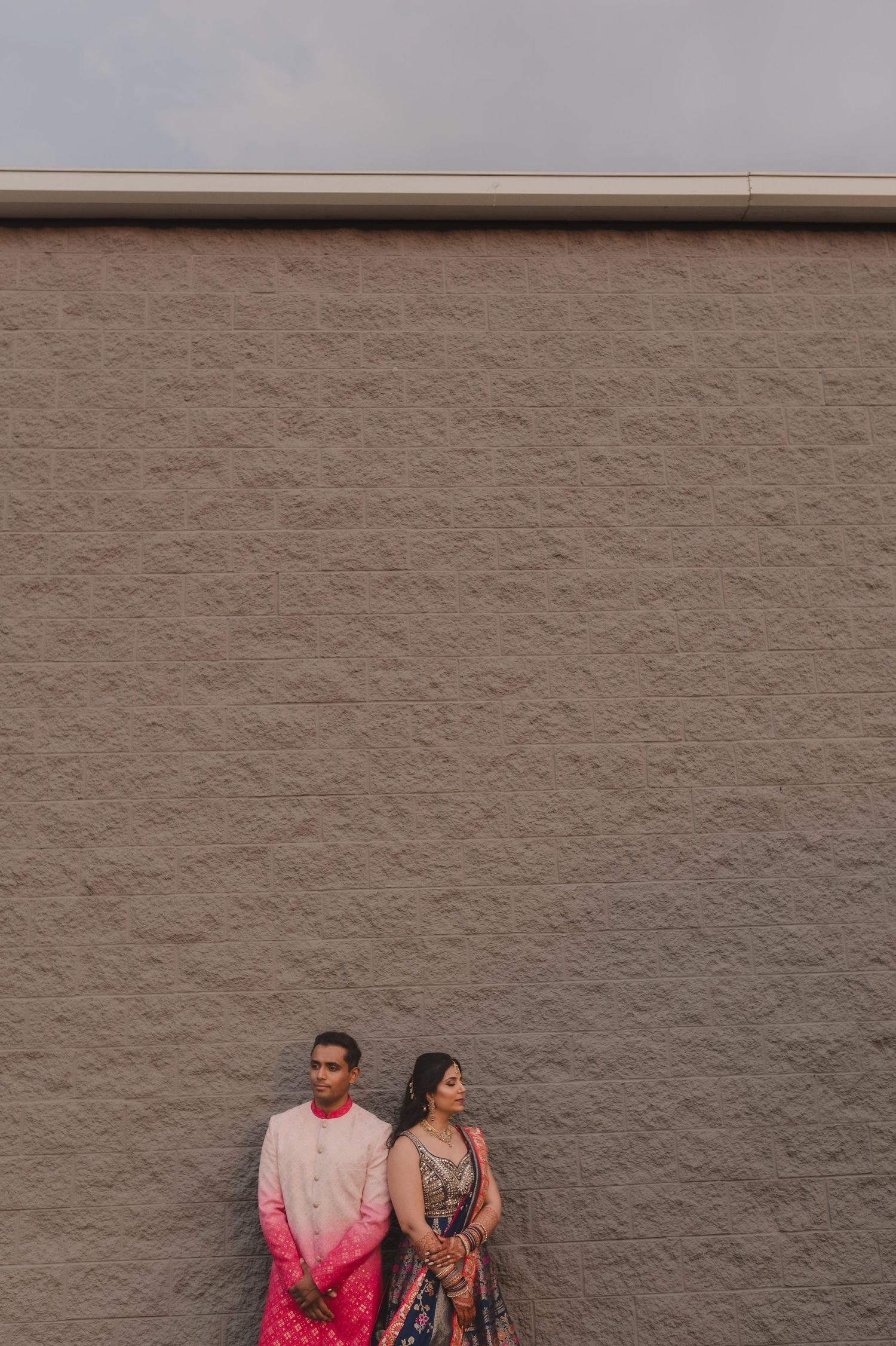 Artistic portrait of a couple against a textured grey wall showing modern fusion wedding attire.