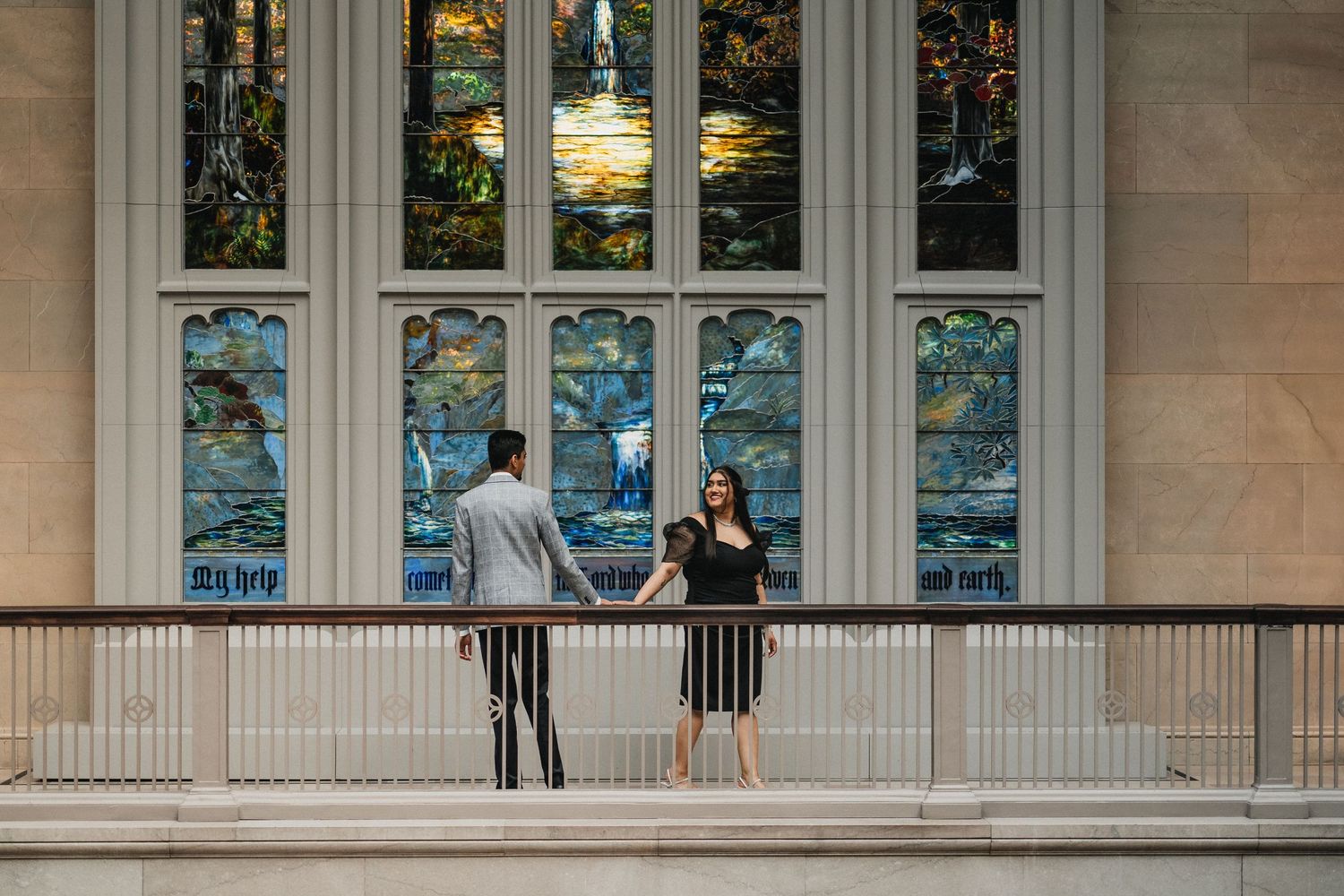 A couple stands by stained glass windows in an elegant architectural setting.