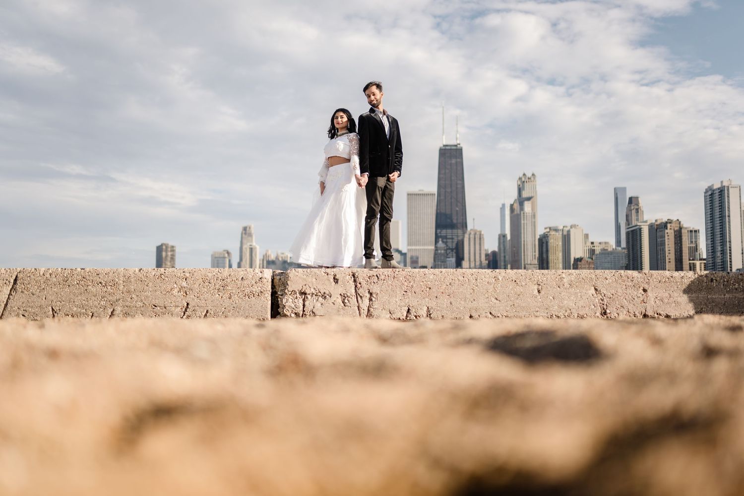 A couple stands on sandy beach with Chicago's iconic skyline in background.