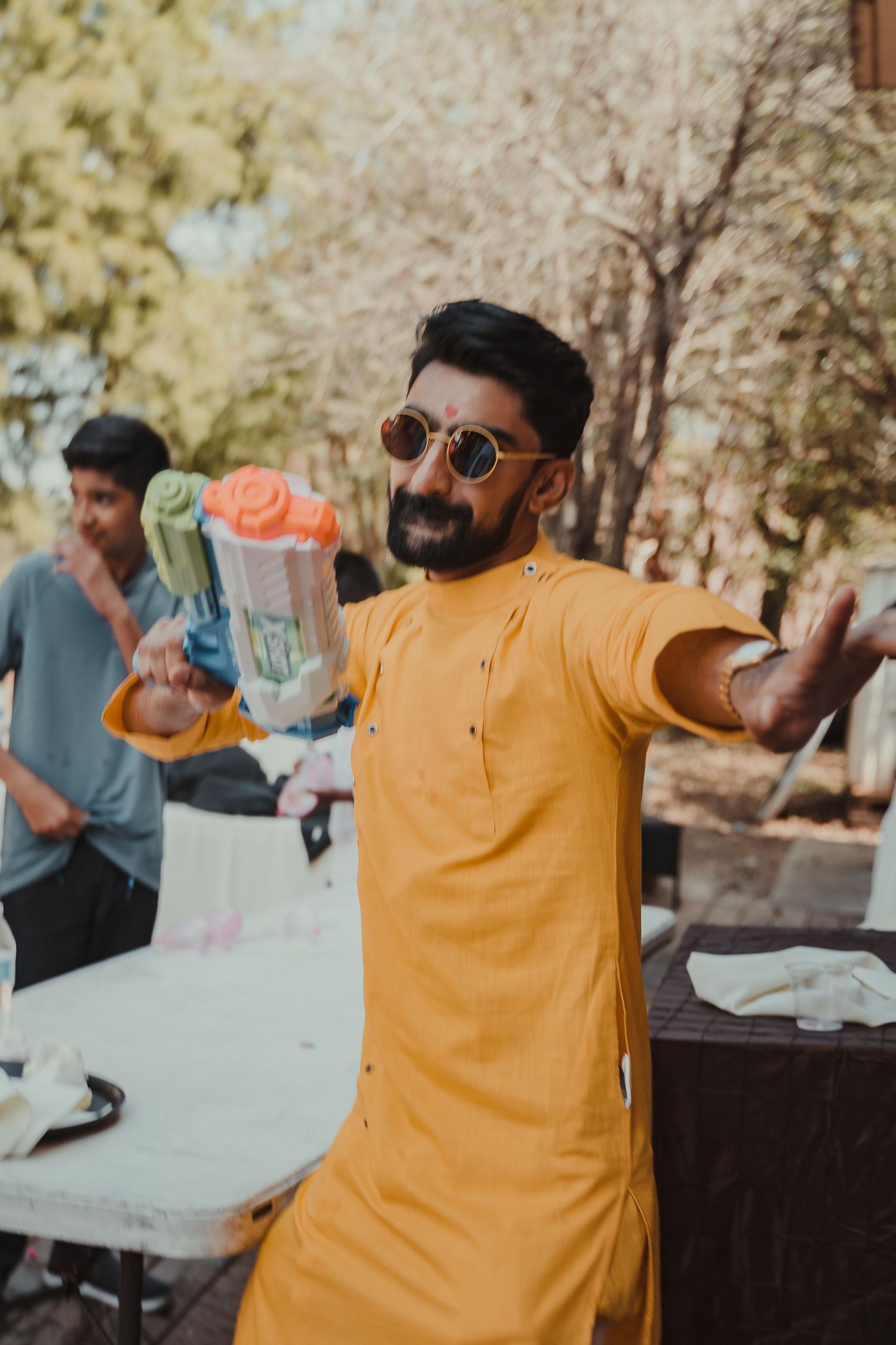 A person in yellow traditional Indian kurta holding a water gun during Holi celebrations.