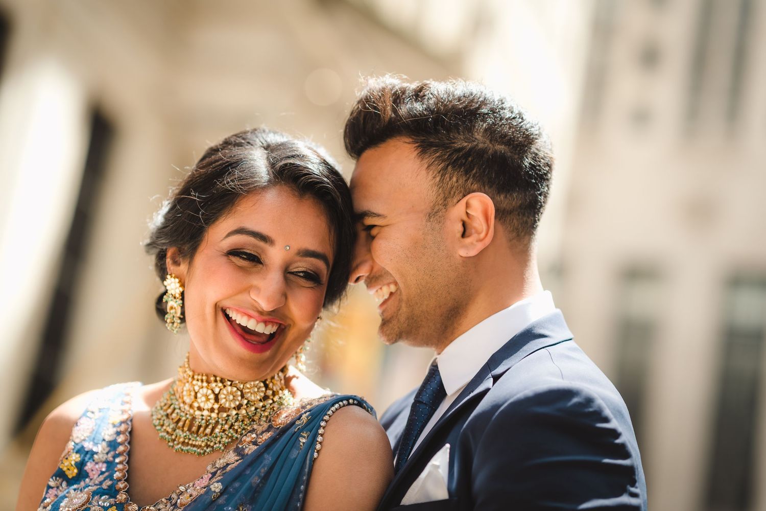 A happy couple shares a romantic moment while wearing traditional Indian and Western wedding attire outdoors.
