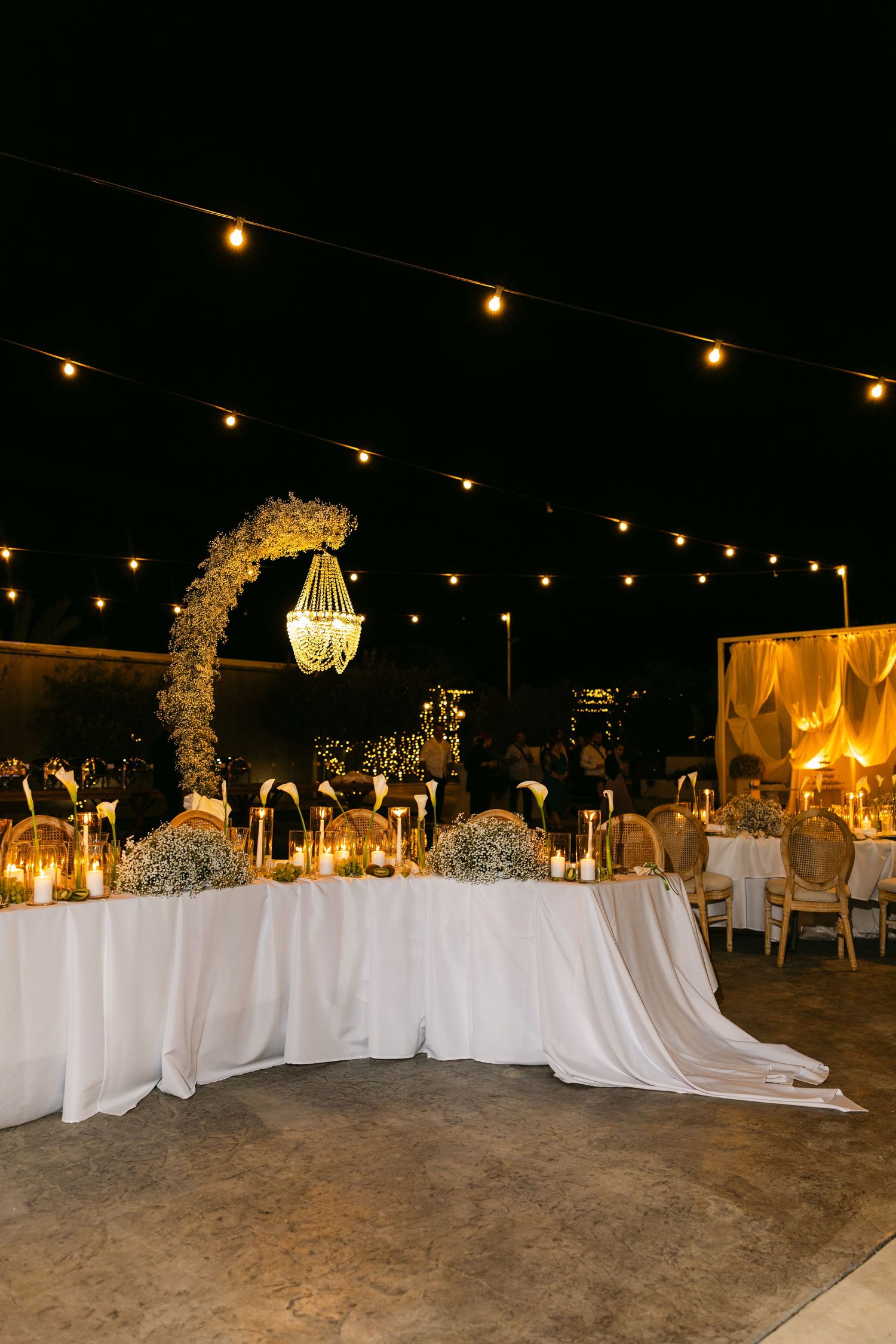 Elegant outdoor wedding reception setup with white tablecloths and string lights under night sky.