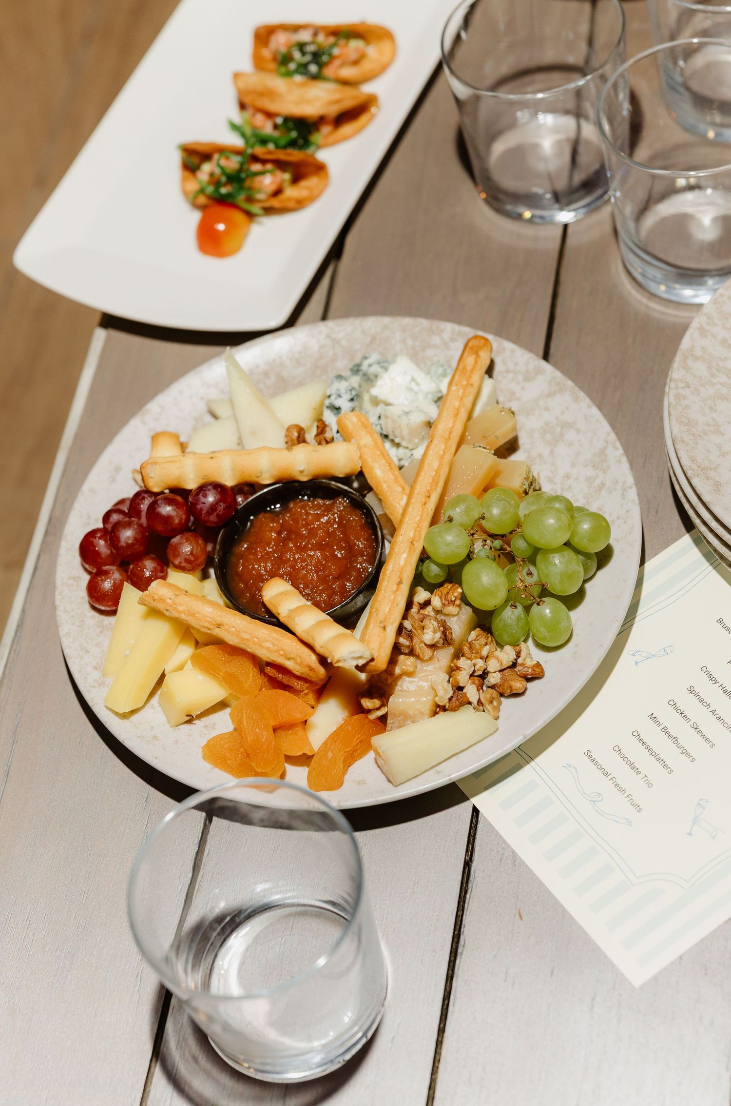 Elegant cheese and fruit platter with crackers and grapes on white plates.