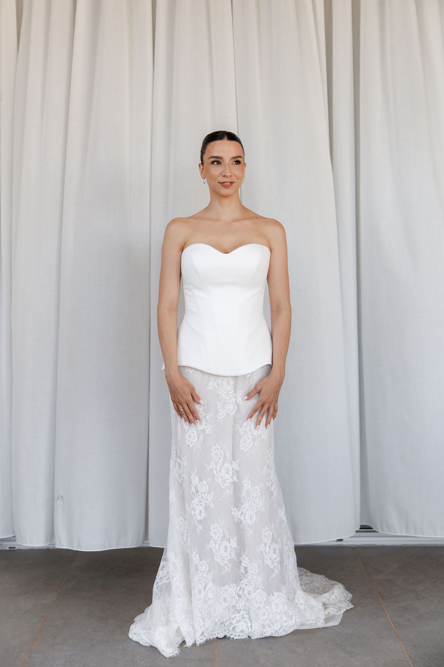 Wedding dress portrait against white curtain backdrop showing strapless bodice and lace skirt details.