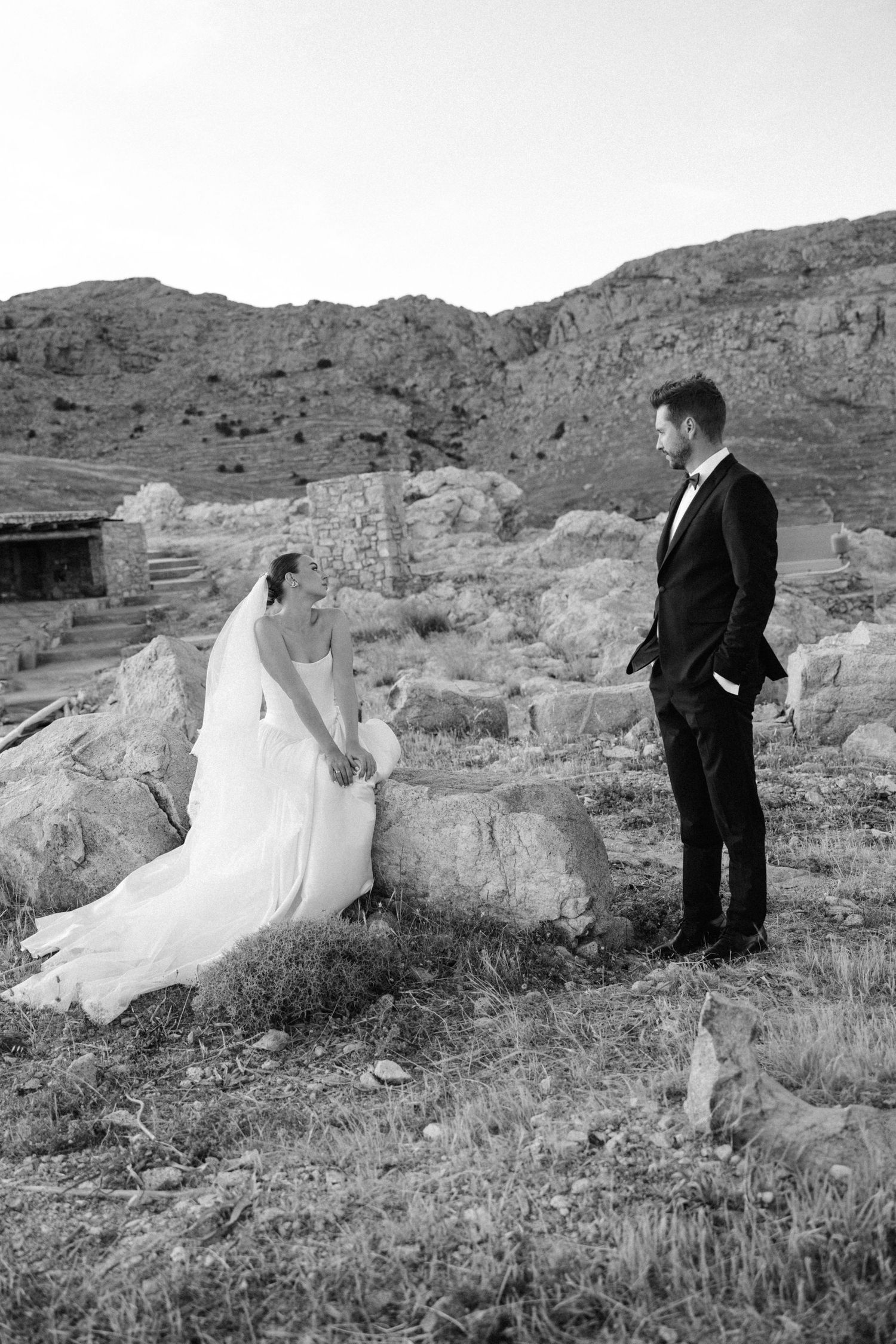 Bride and groom share a romantic moment among ancient ruins in a black and white outdoor photo.