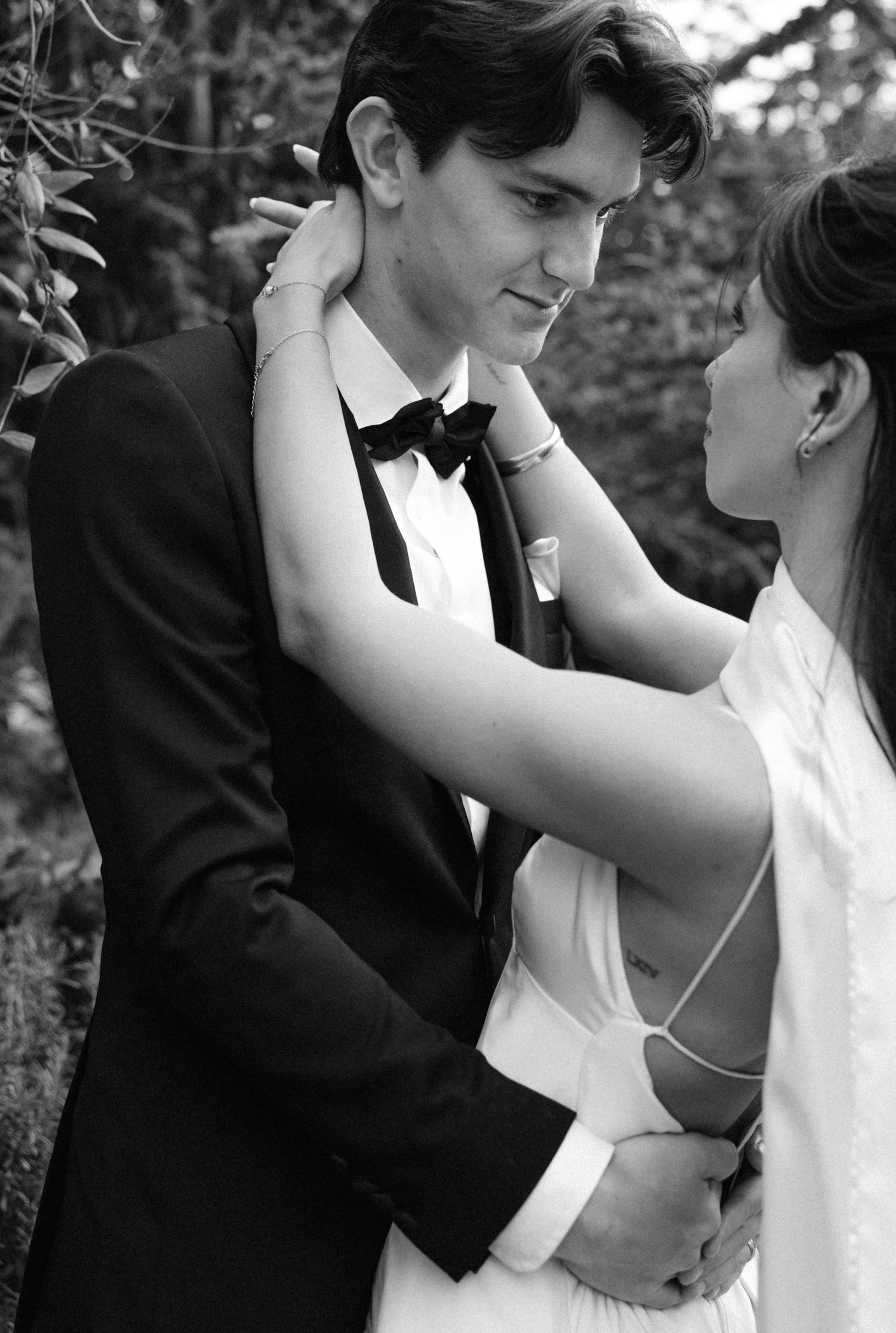 Black and white photo of intimate wedding couple moment with bride in flowing dress and groom in tuxedo.