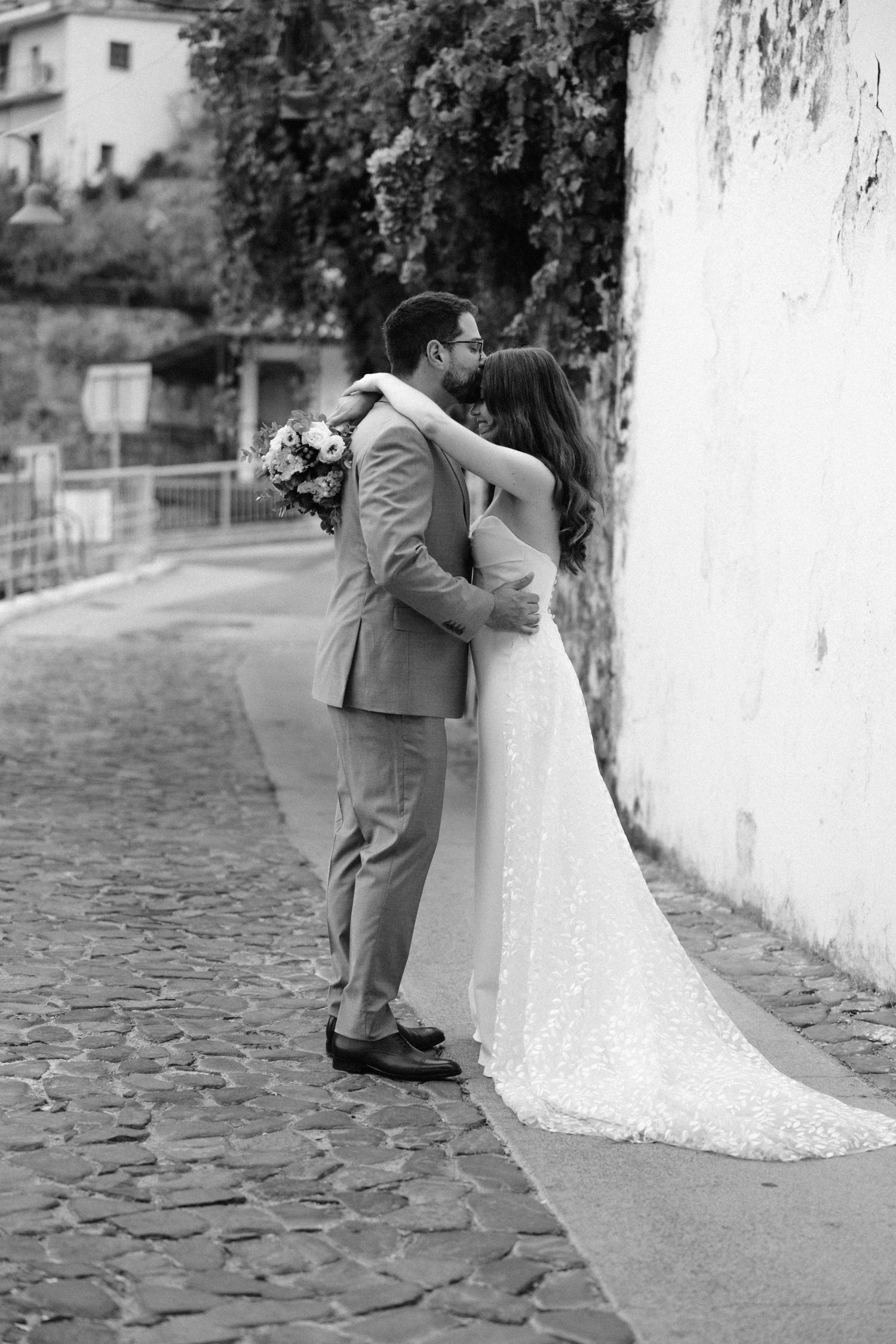 Black and white romantic portrait of newlyweds embracing on cobblestone path.