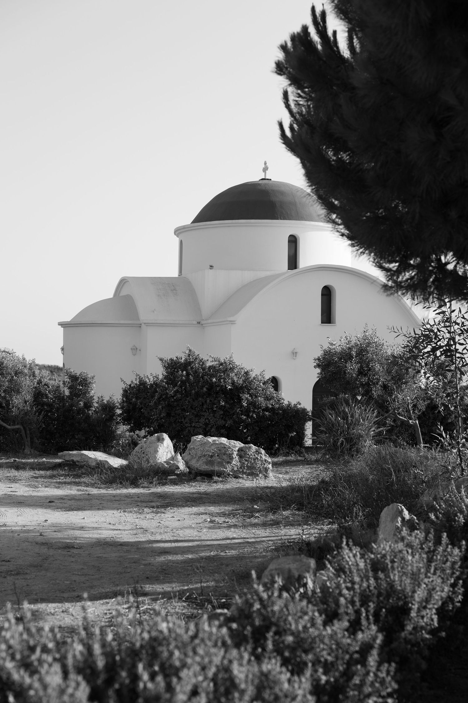 Black and white photo of a white domed Greek Orthodox church surrounded by trees and rocks.