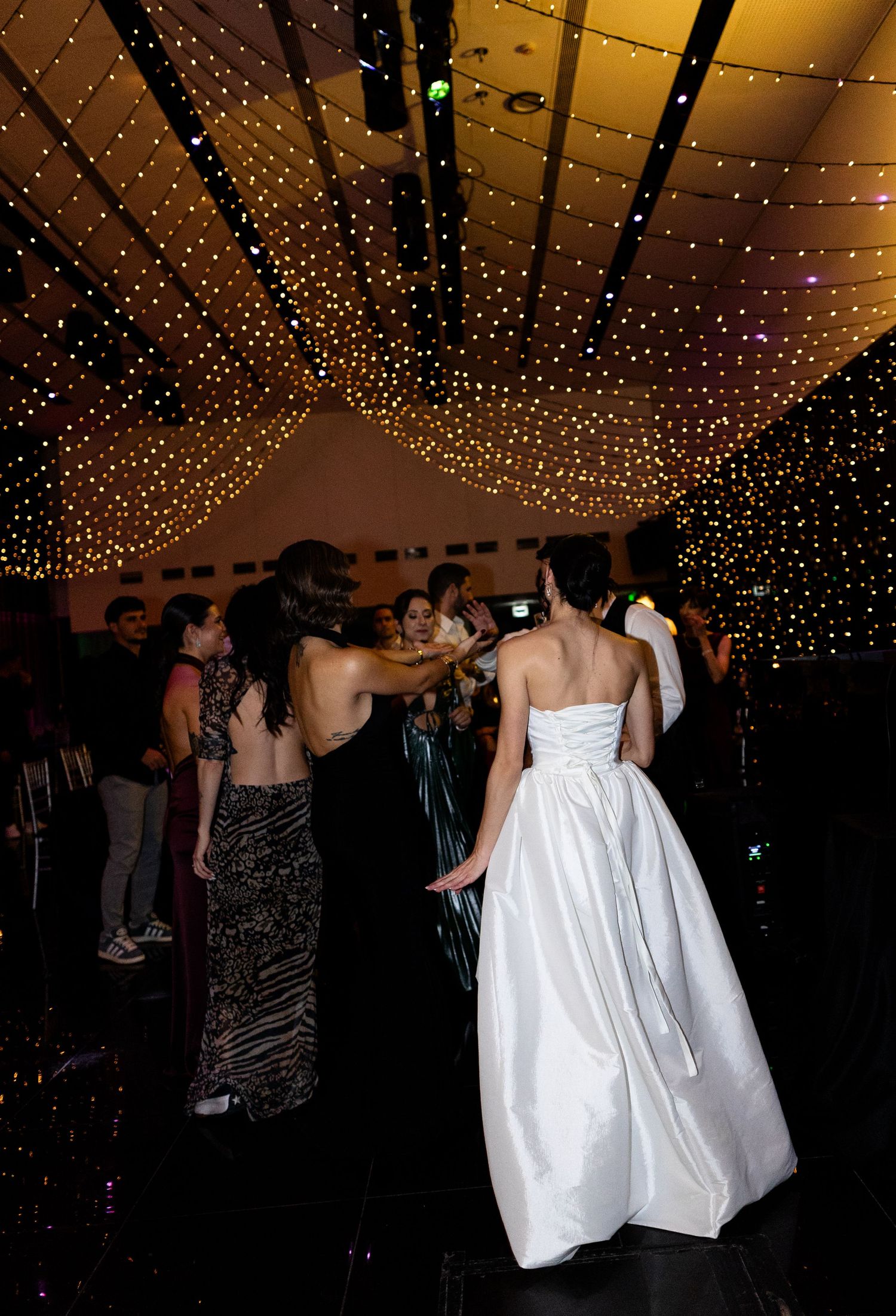 A bride in a strapless white ball gown dances under a stunning starlit ceiling at a wedding reception.