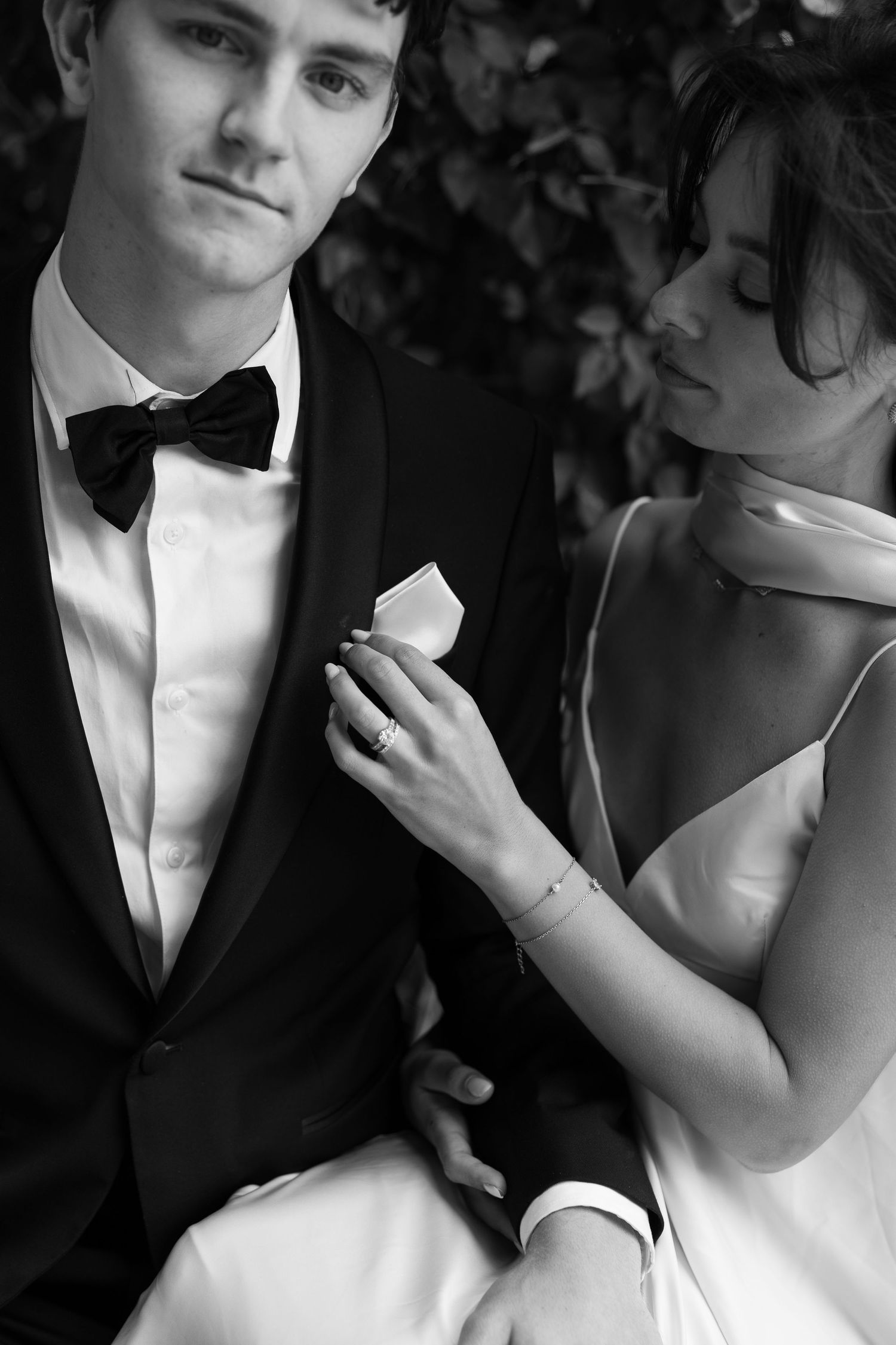 Close-up black and white photo showing details of formal wedding attire and intimate moment.