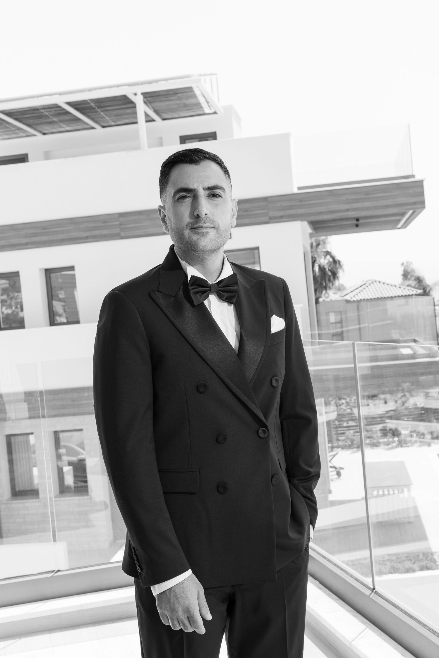 Professional wearing a dark business suit stands in modern office hallway with glass windows and natural light.