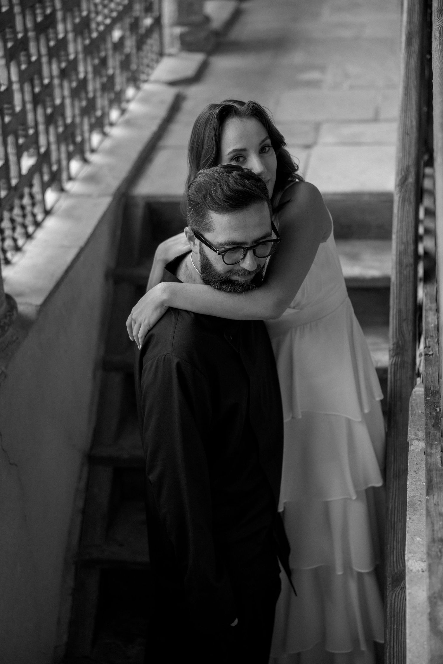 A black and white stairway portrait captures a tender moment between a couple.
