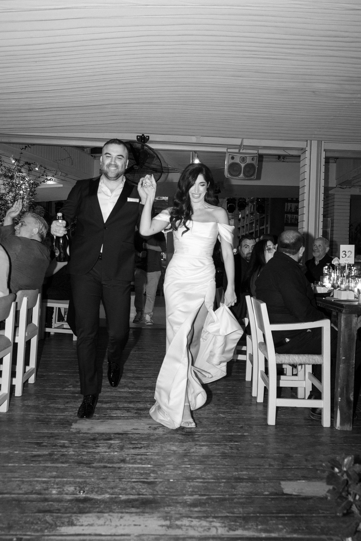 Bride and groom walking joyfully into wedding reception in black and white photo.