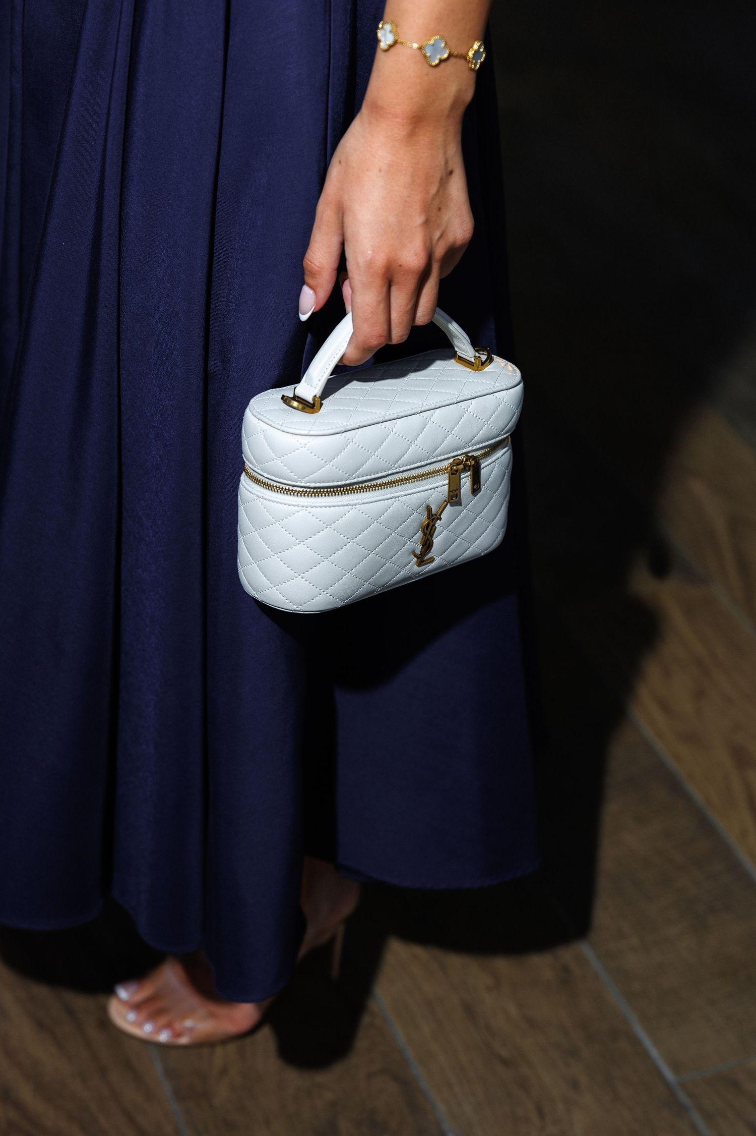 Close-up of quilted white handbag and bracelet against navy dress.