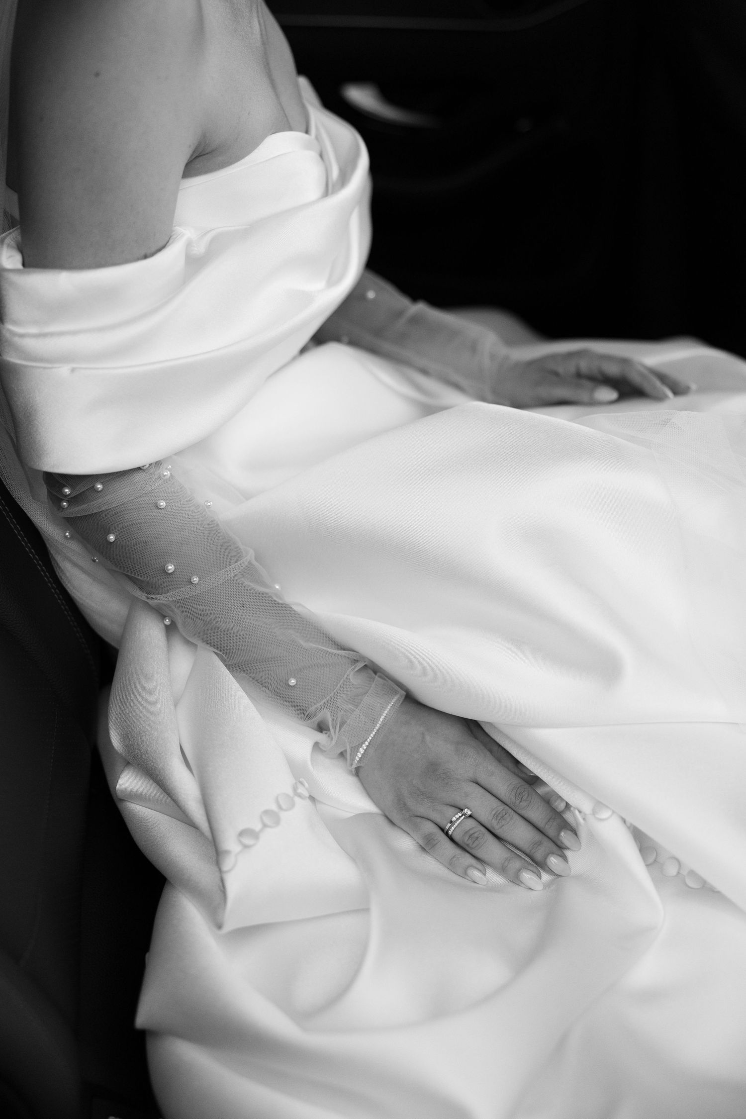 Black and white photo of a bride in a white gown with lace gloves and a ring, hands resting on her dress.