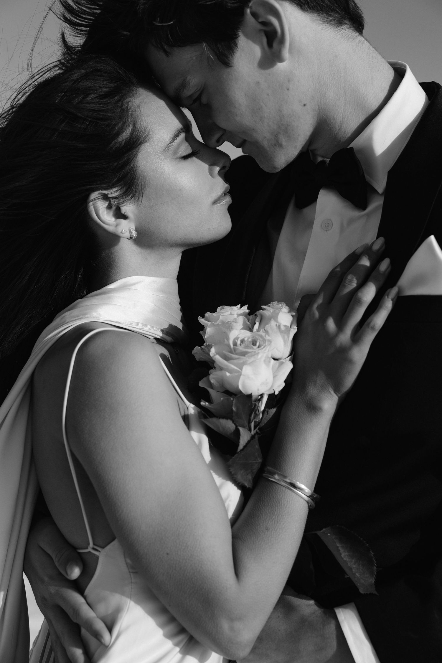 A romantic black and white portrait of a couple embracing with a white rose corsage.