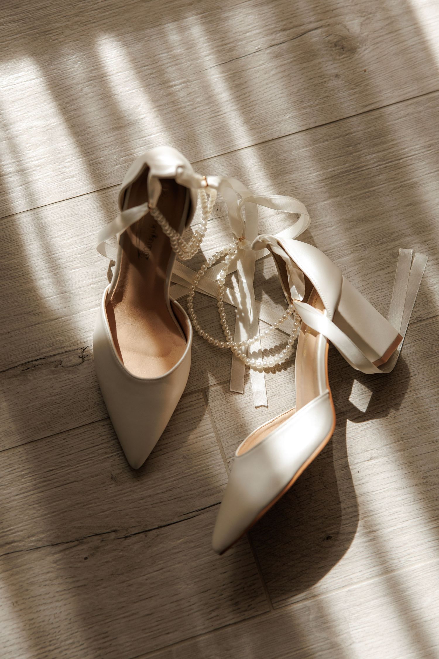 White bridal shoes with ribbon details photographed in natural window light.