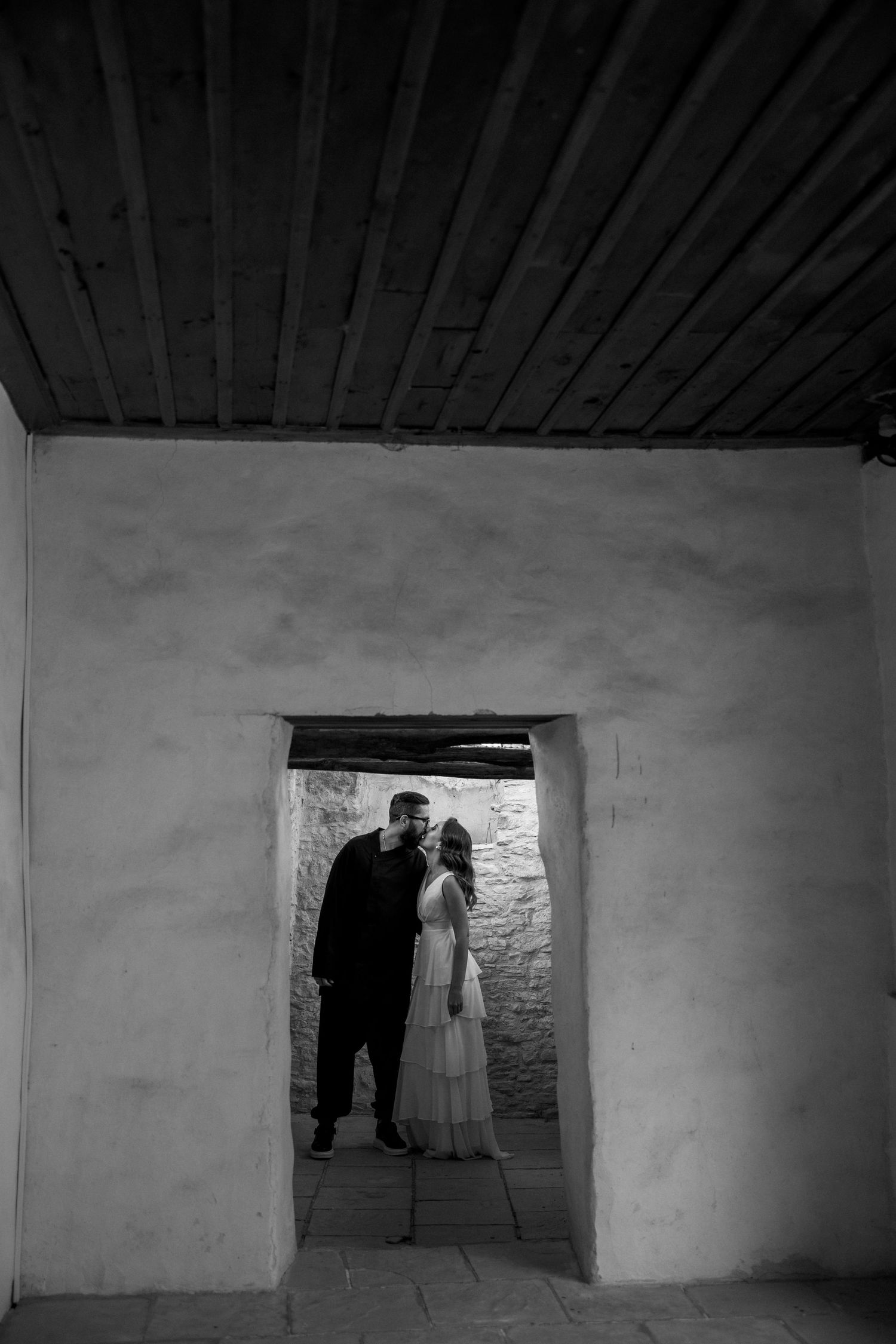 A silhouetted couple stands in a stone doorway creating a dramatic black and white wedding portrait.