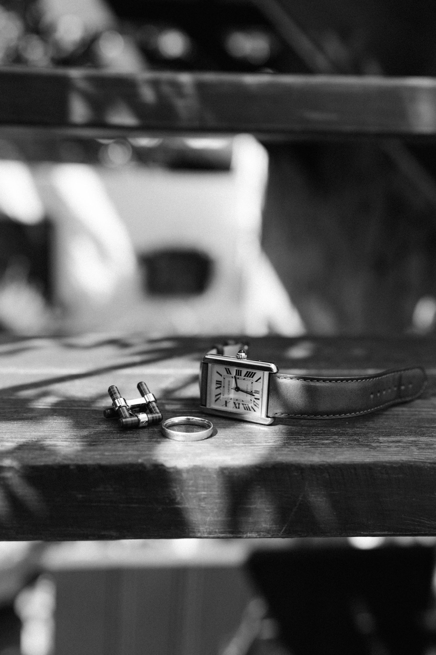 A black and white still life of a vintage watch, ring, and cufflinks arranged on a wooden surface in soft lighting.