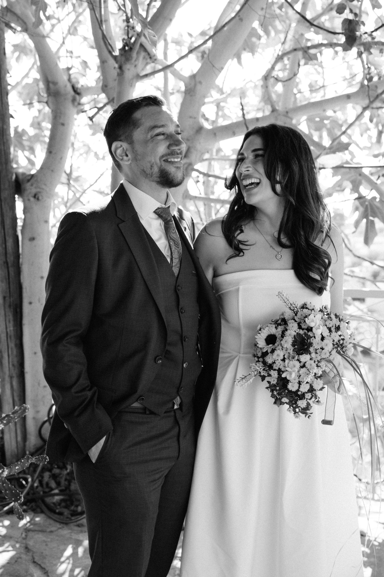 A candid wedding moment captured in black and white beneath blooming trees.