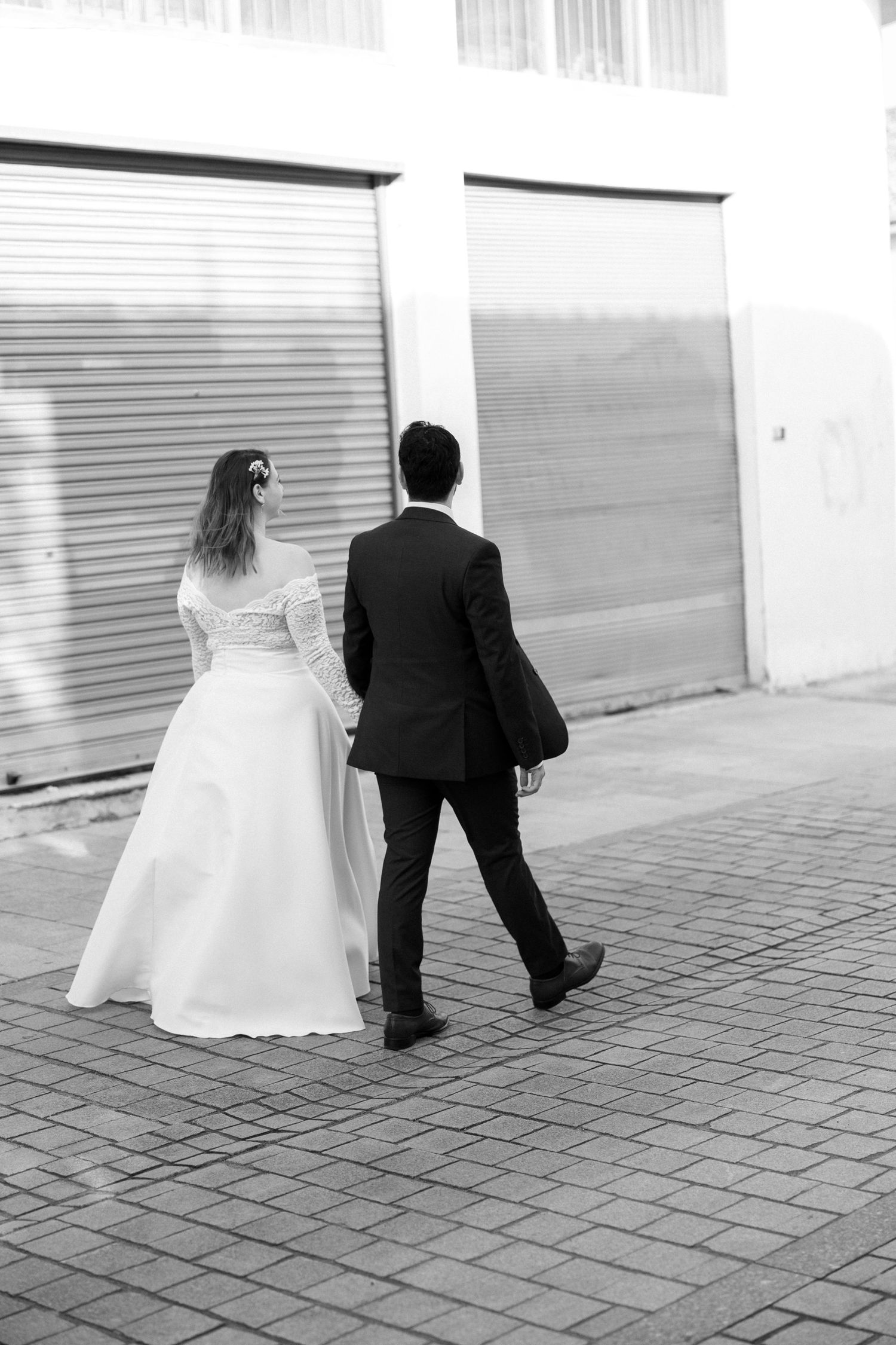 Black and white photo of bride and groom walking hand in hand on cobblestone street.