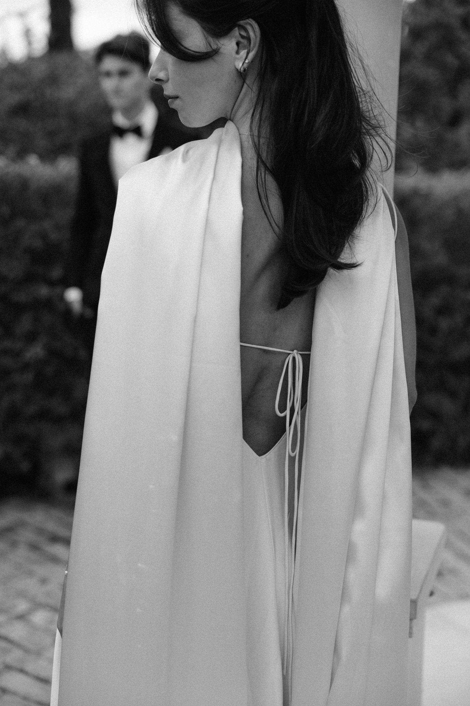 Elegant black and white wedding photo showing a flowing white dress with delicate straps and cape details.