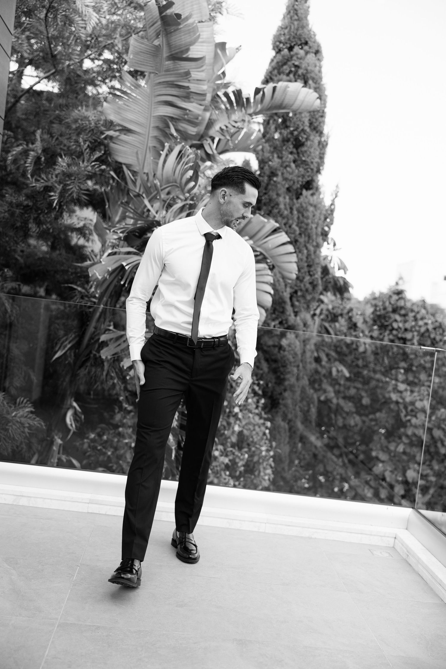 Black and white photo of a man in formal attire standing by tropical plants.