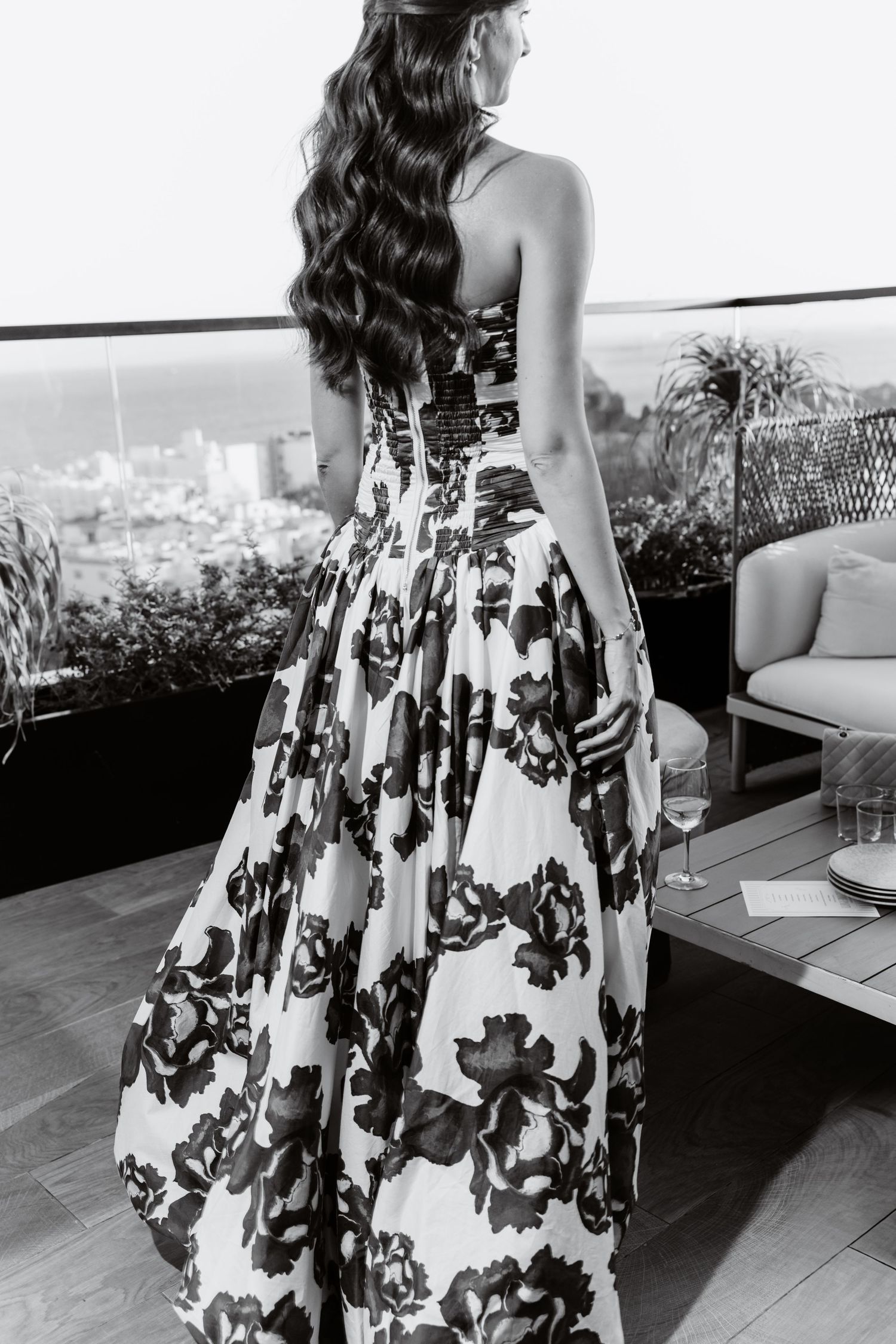 A woman in a floral print dress poses against a scenic city backdrop.