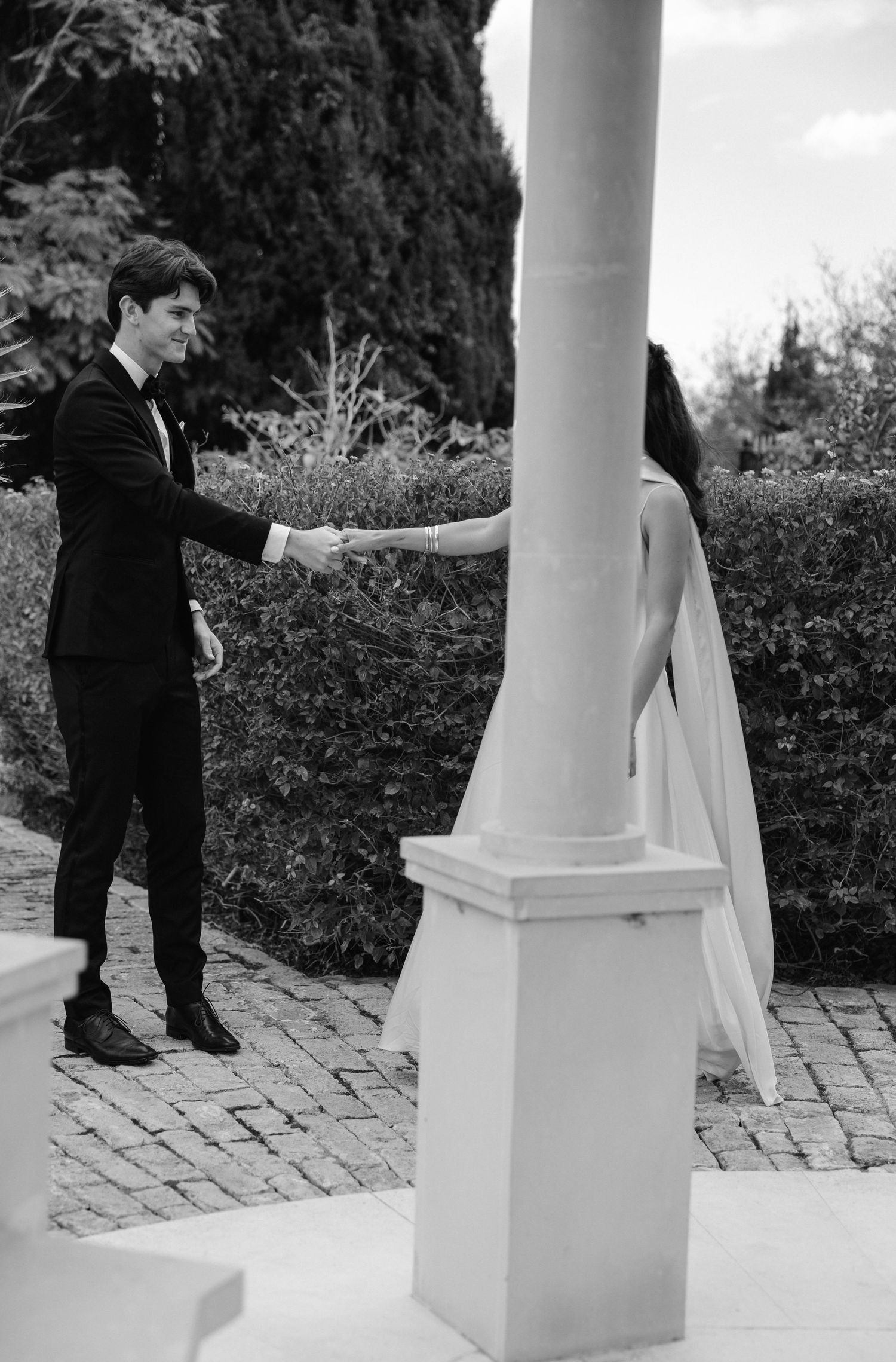 Black and white photo of a couple meeting on a porch with white columns and brick paving.