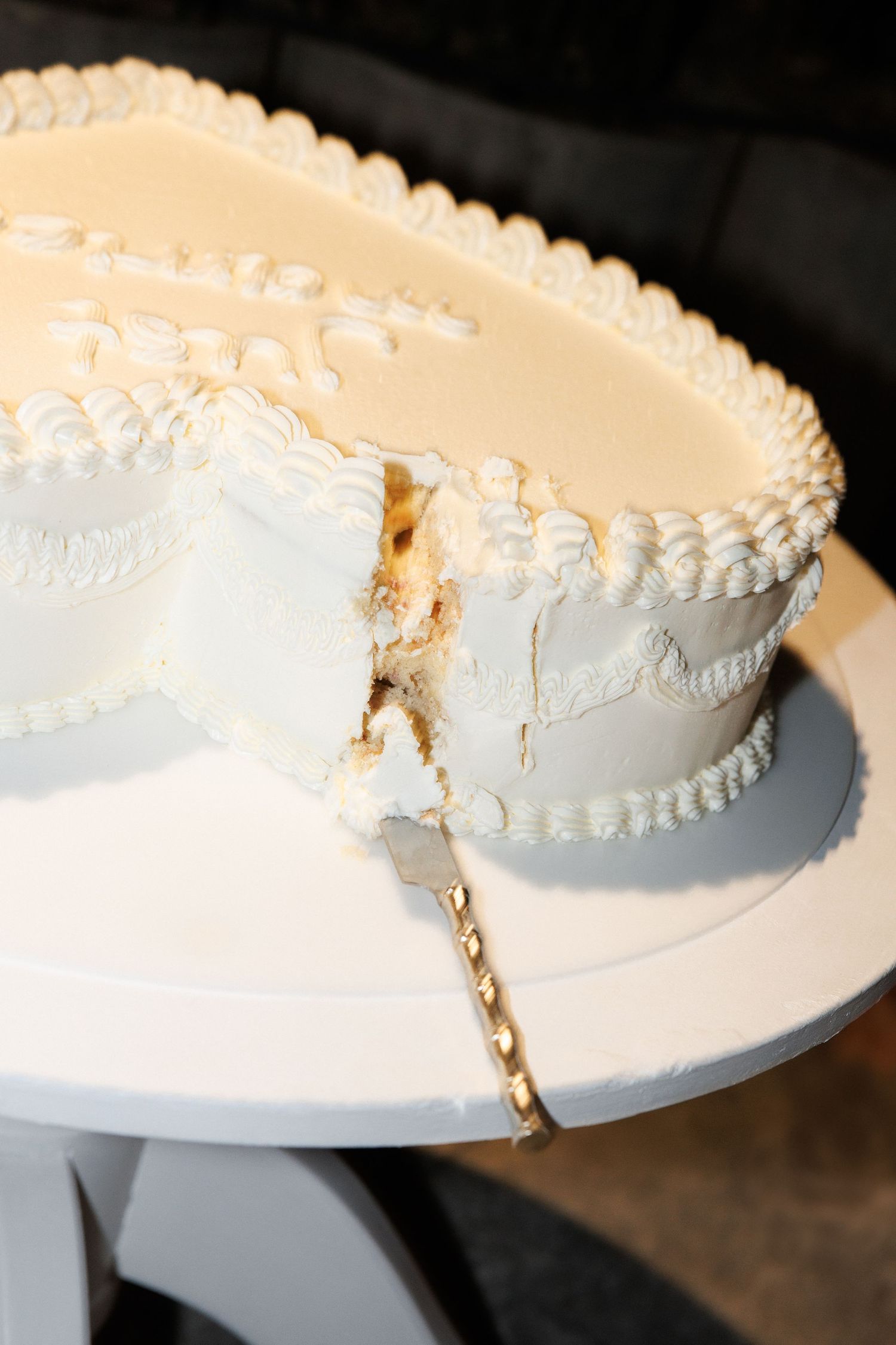 A classic white wedding cake with piped decorative borders sits sliced on a round plate.