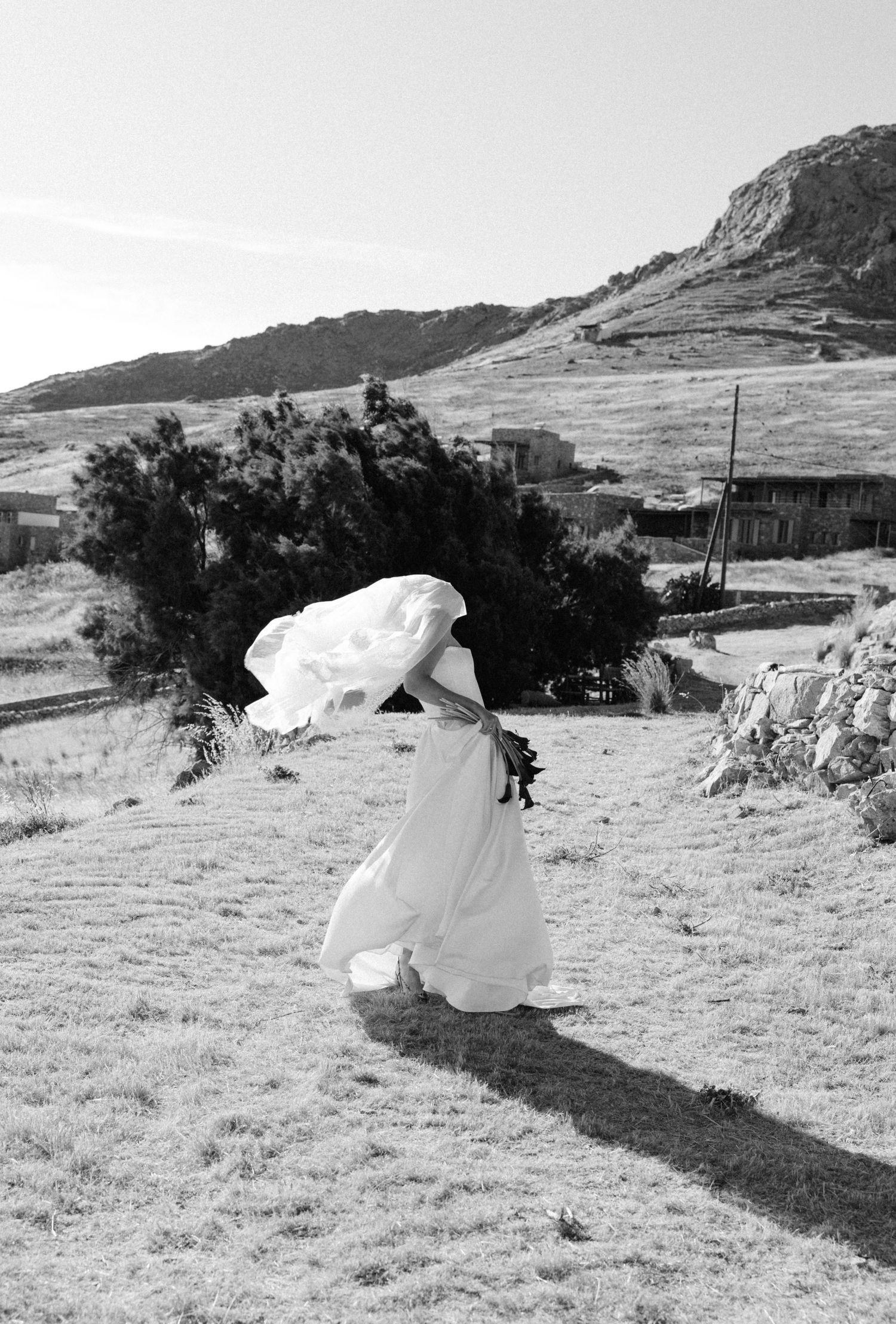 Bride in white gown walking through windy hillside landscape in black and white wedding photo.