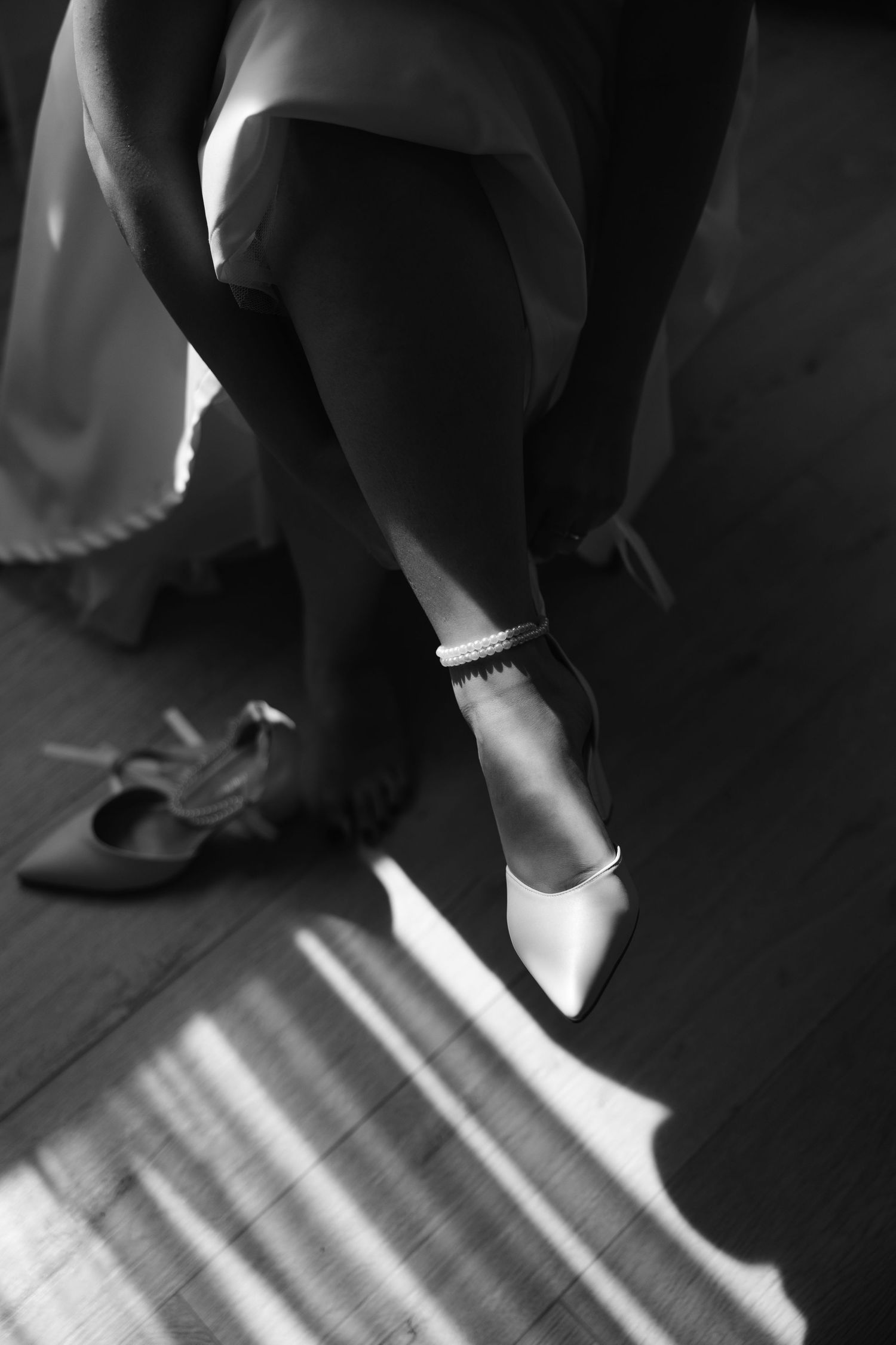 A black and white detail shot of elegant bridal shoes and anklet.