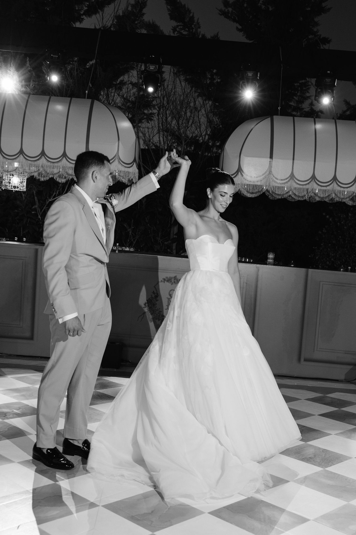 A couple dancing on a checkered floor at their wedding reception in black and white.