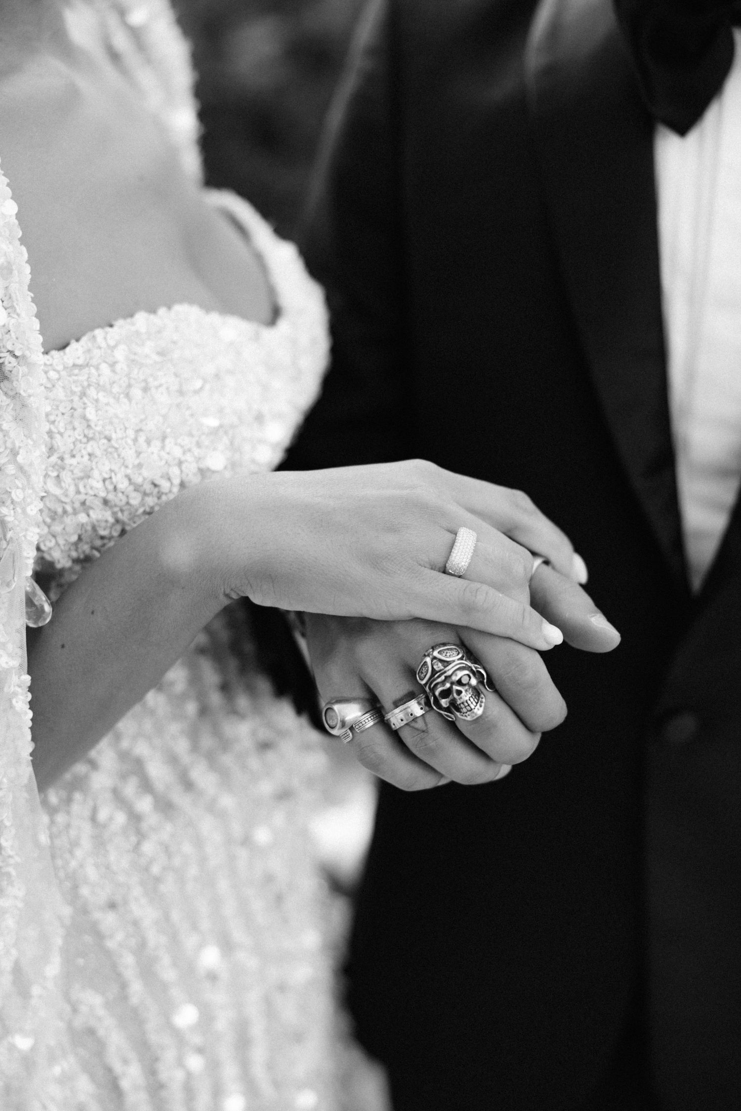 Close-up black and white photo of bride and groom holding hands showing wedding rings.