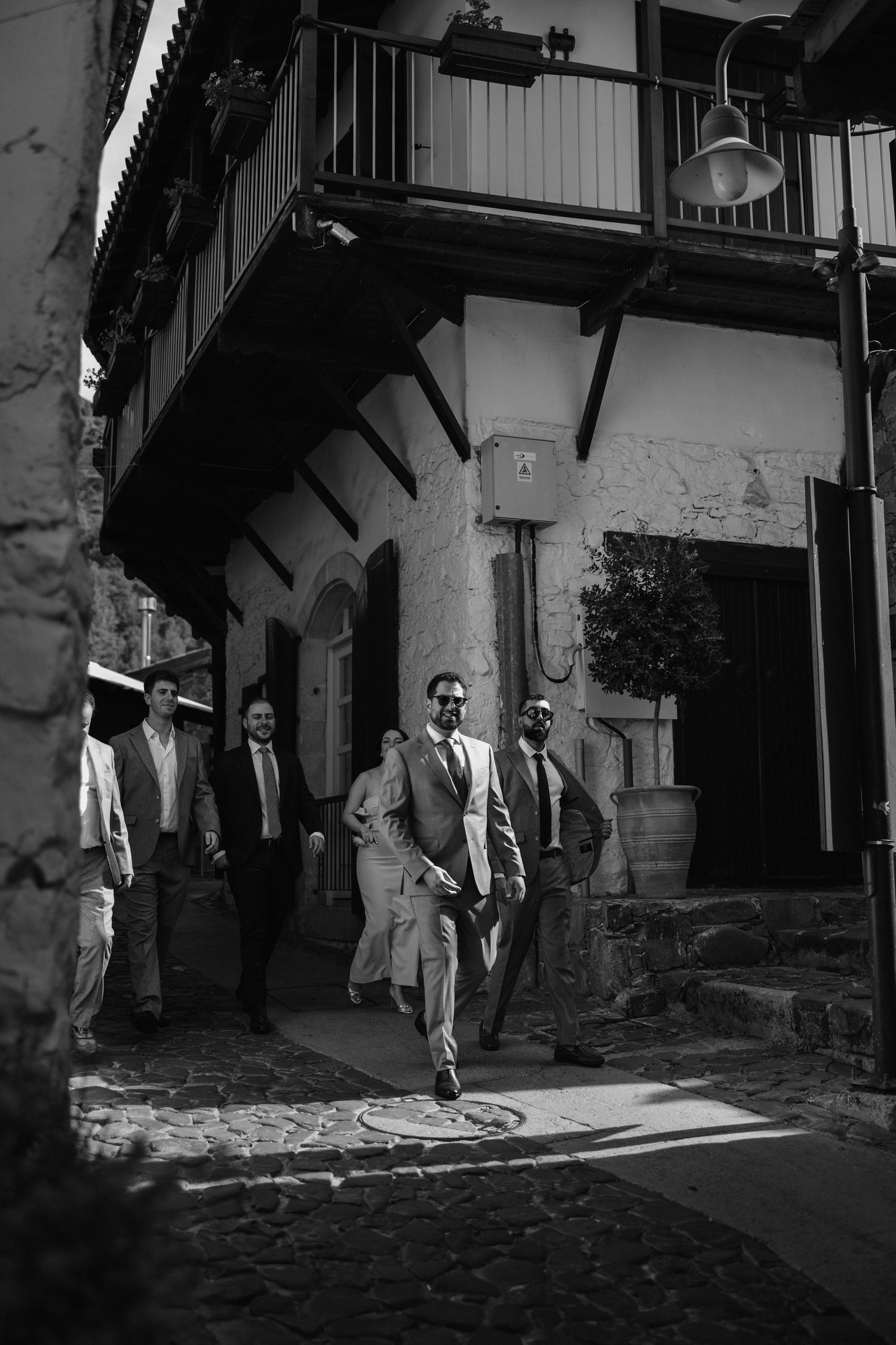 Black and white photograph showing a group walking under an arched architectural entryway on a cobblestone street.