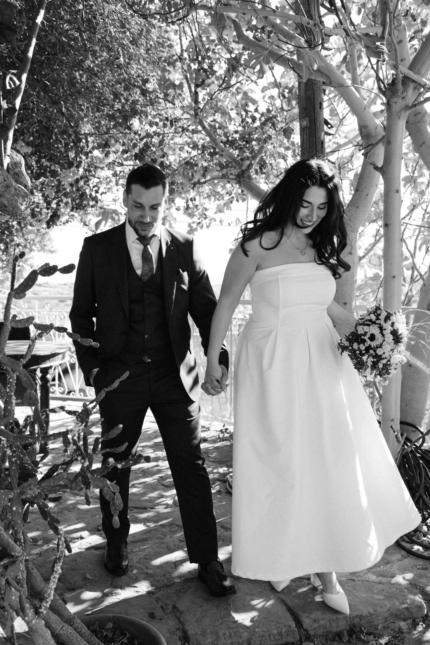 A playful wedding photoshoot in a garden setting with dappled sunlight through the trees.