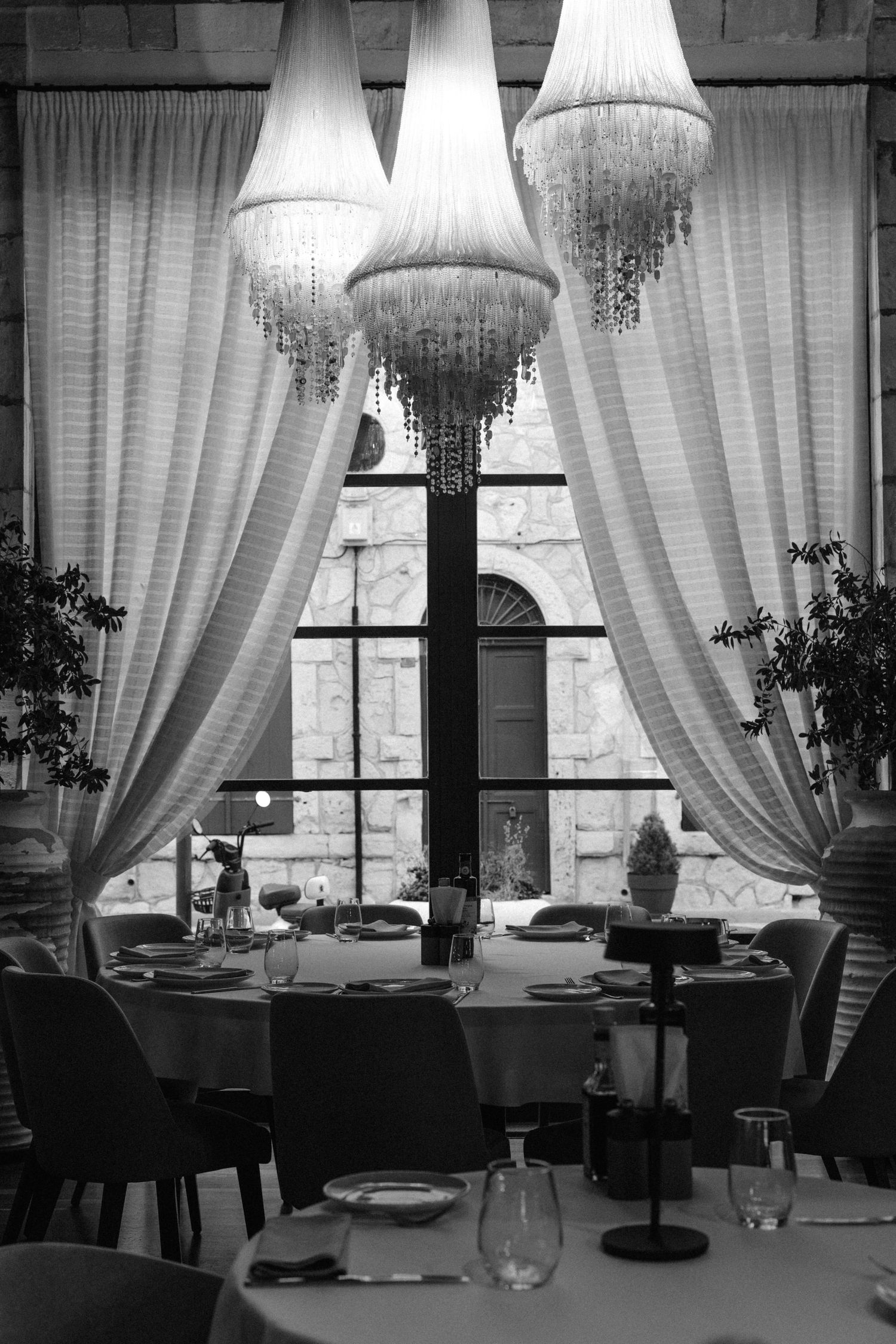 A black and white series of windows in a restaurant interior featuring elegant white curtains and chandelier lighting.