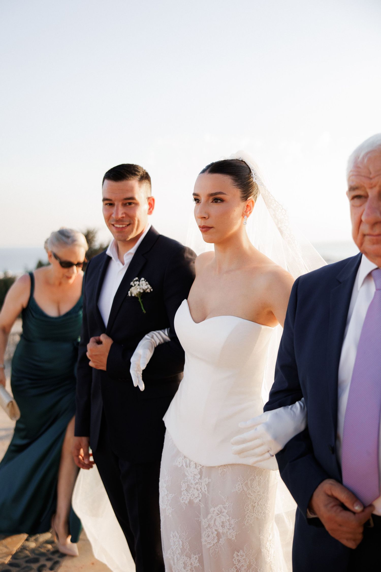 Wedding party gathering outdoors in formal attire with white gown in focus.