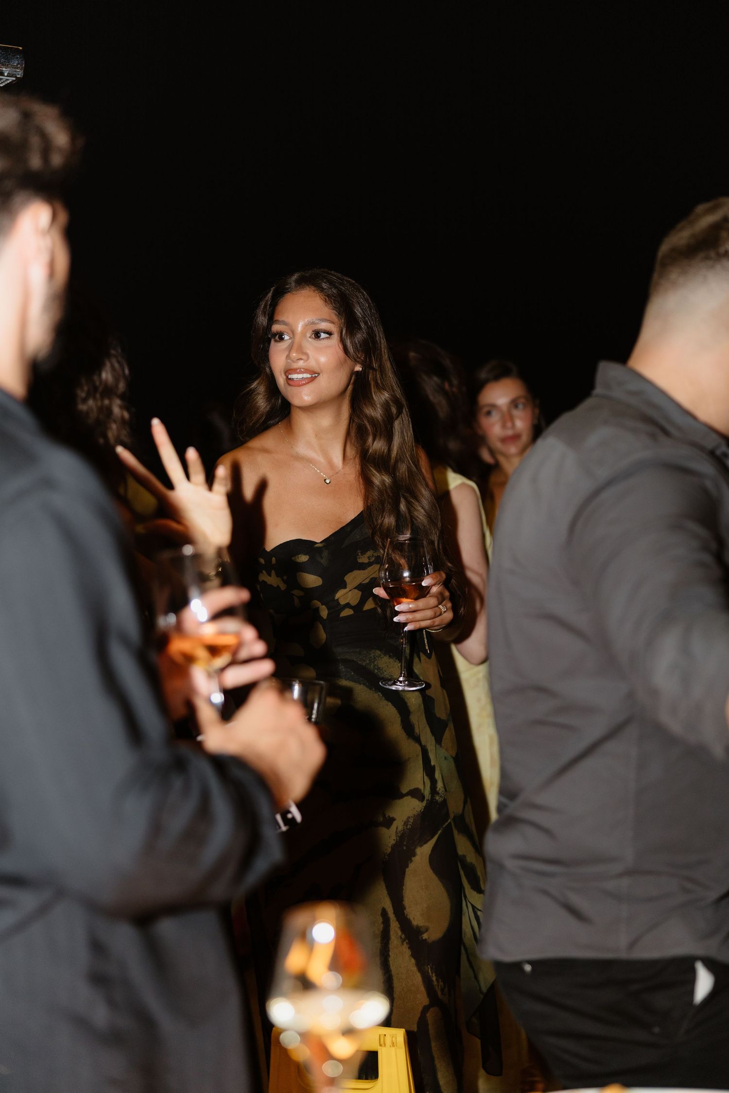 A lively nighttime gathering shows guests in elegant attire mingling at an upscale event.