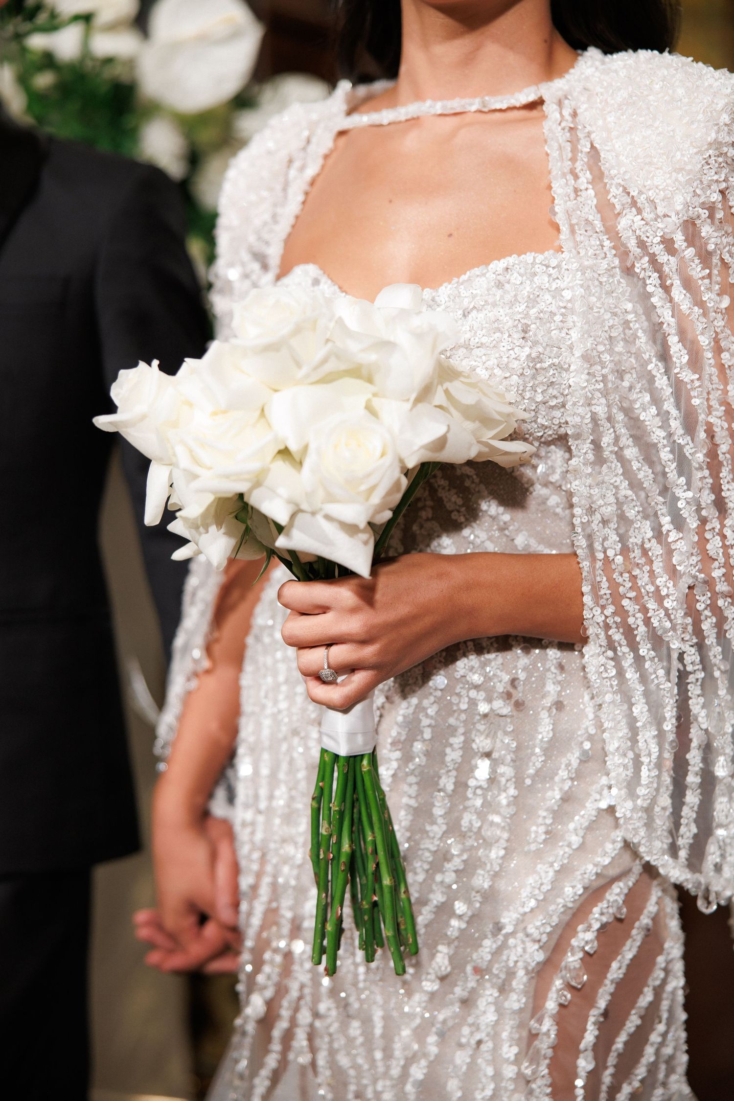 Bride in a sequined wedding dress holding a bouquet of white roses during a wedding ceremony.