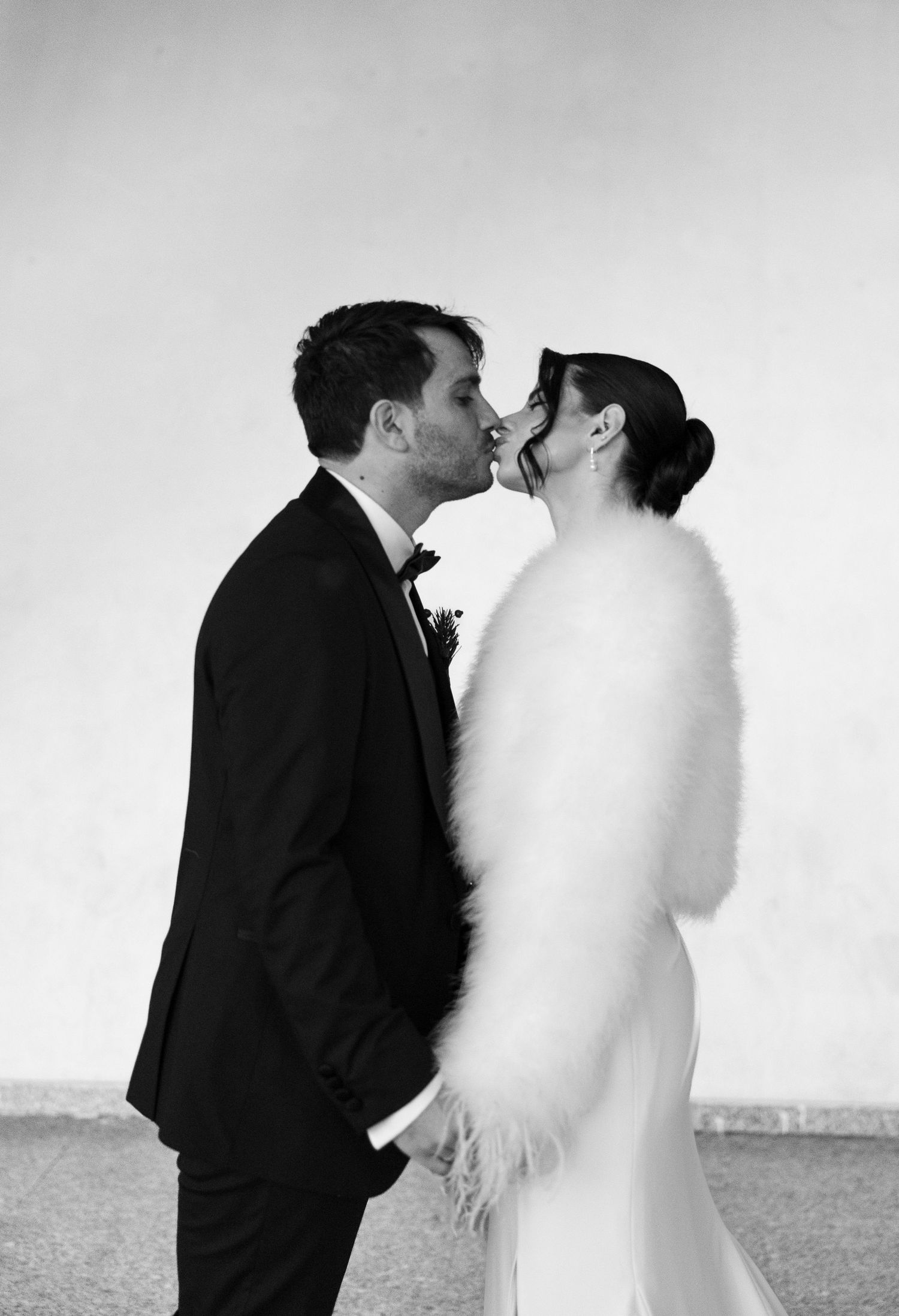 Black and white photo of a bride and groom sharing a kiss, she wears a fluffy white fur stole over her wedding dress.