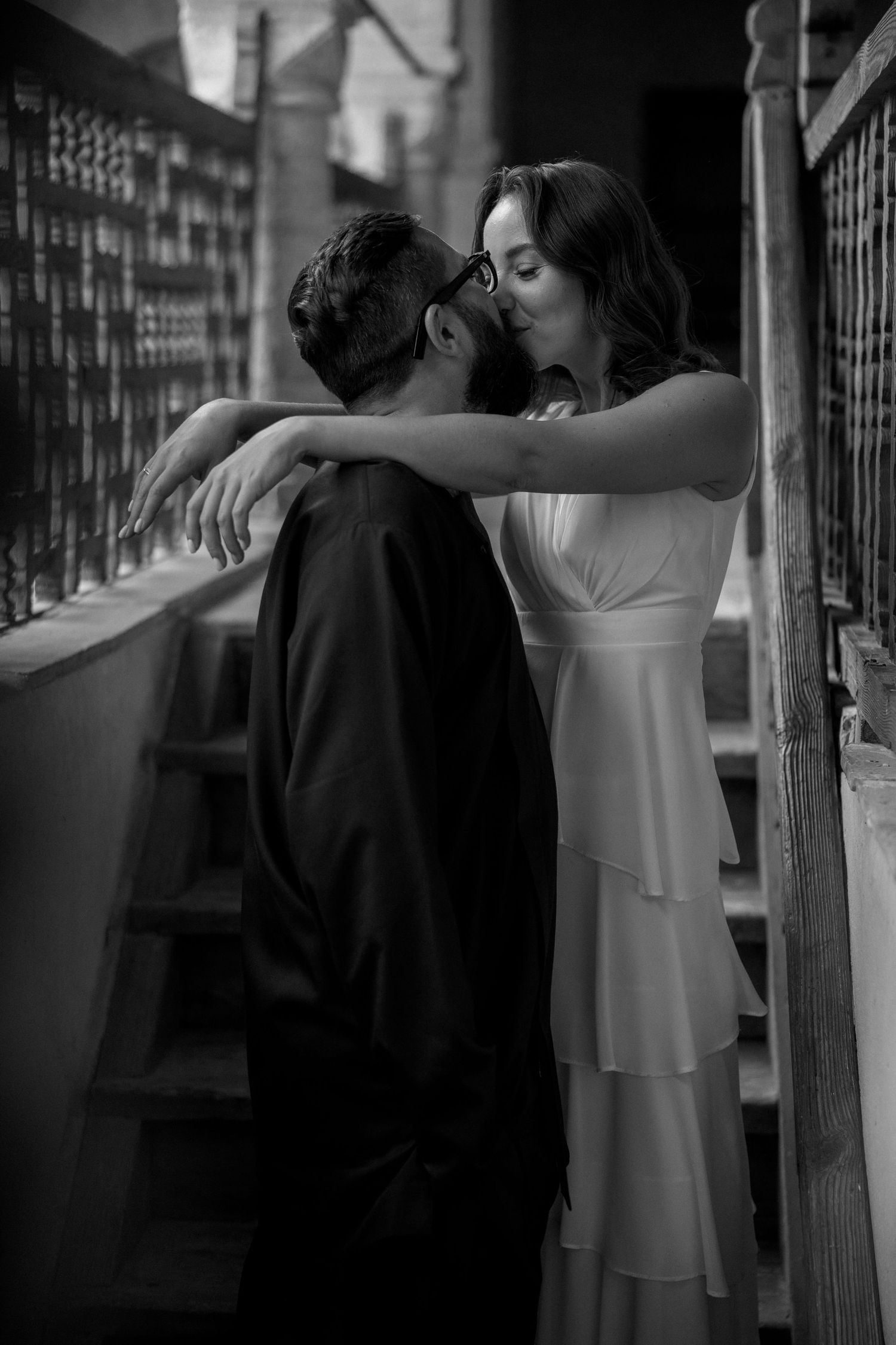 An intimate black and white portrait of a couple sharing a tender moment on stairs.