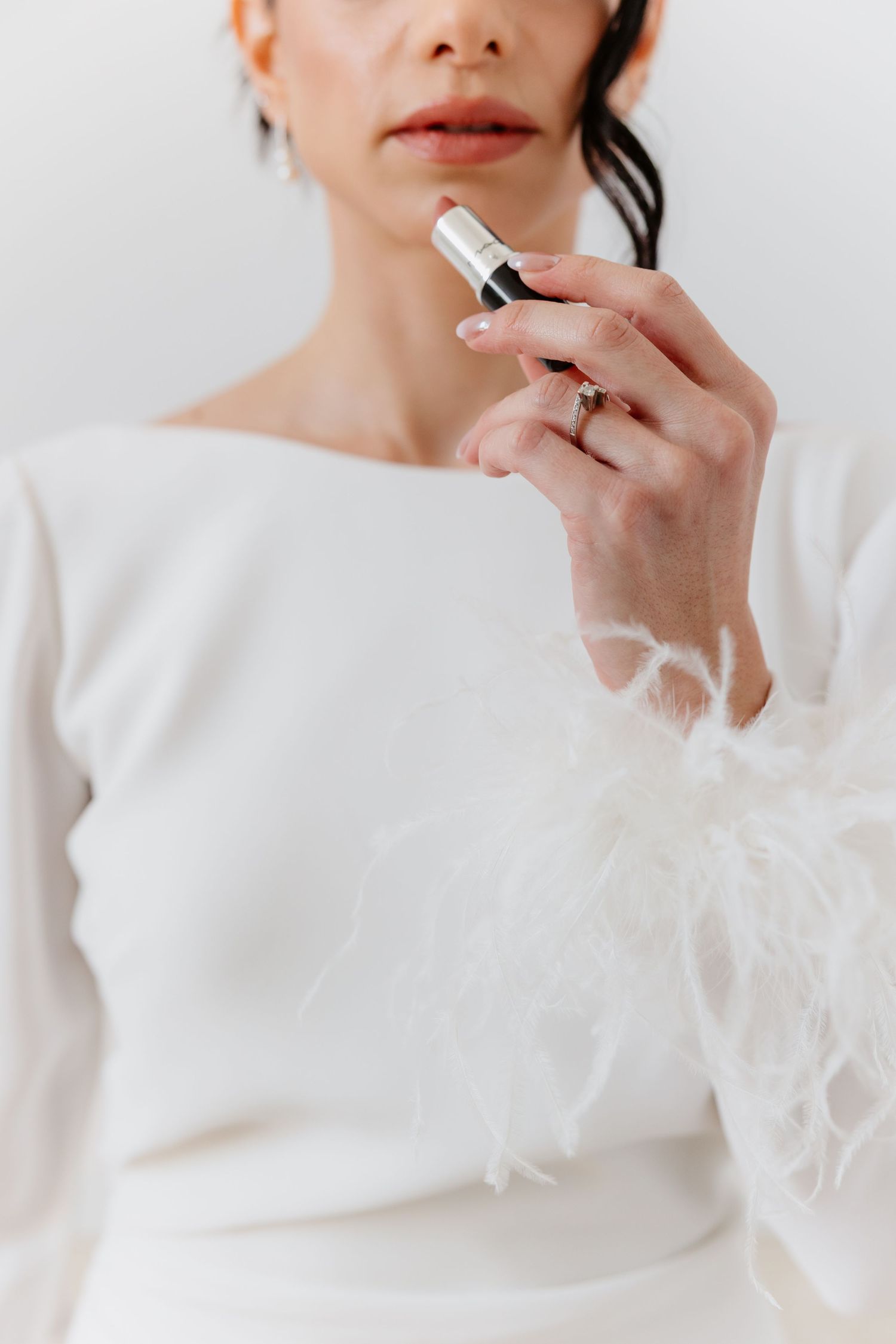 Bride in white feather-cuff dress holding a perfume travel spray.