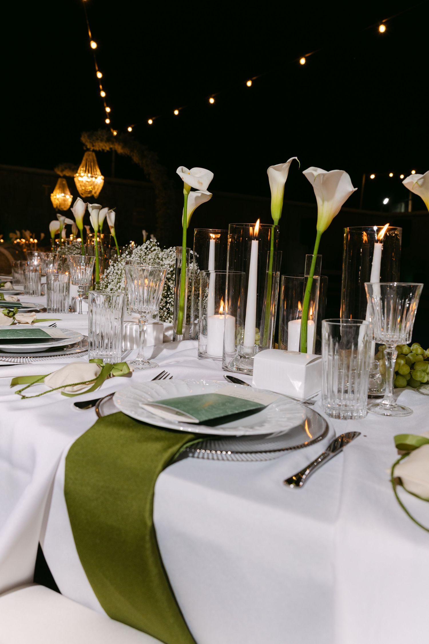 Elegant wedding reception table setting with green accents and crystal glassware.