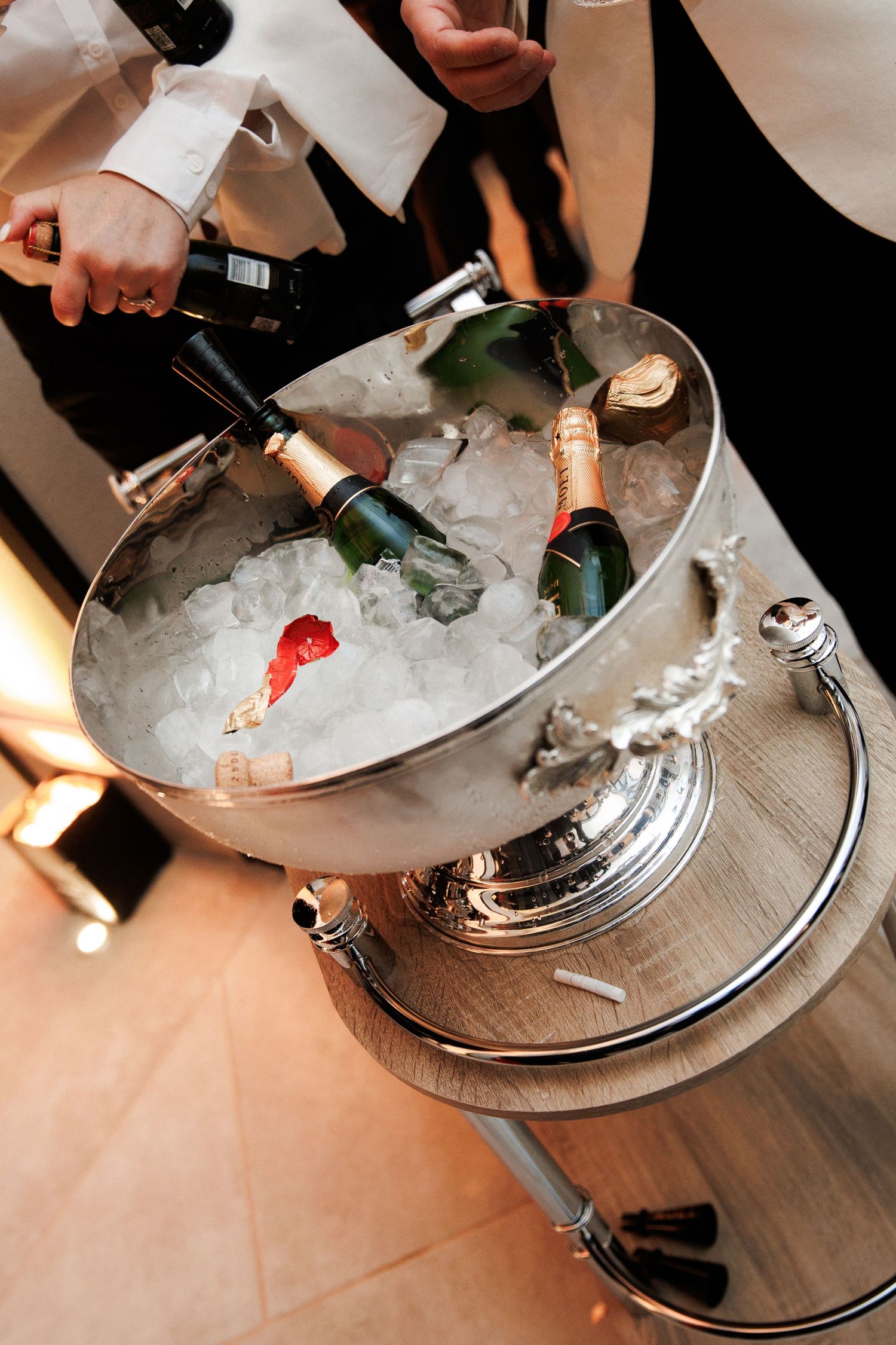 Elegant silver champagne bucket filled with ice and bottles, attended by waitstaff at a formal event.